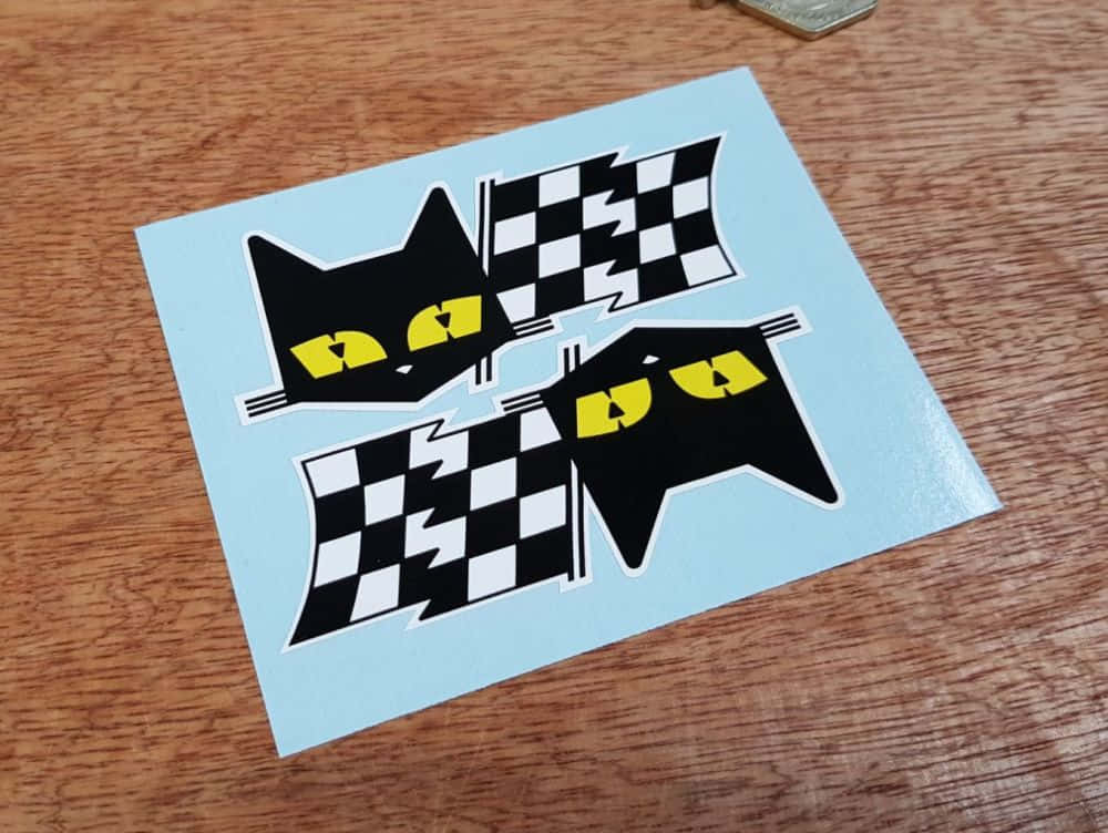 Chequered Flag 桌布 壁紙 — 兩張黑色貓咪貼紙，黃色眼睛，帶有方格旗，放在淺藍色紙張上，置於木質表面。