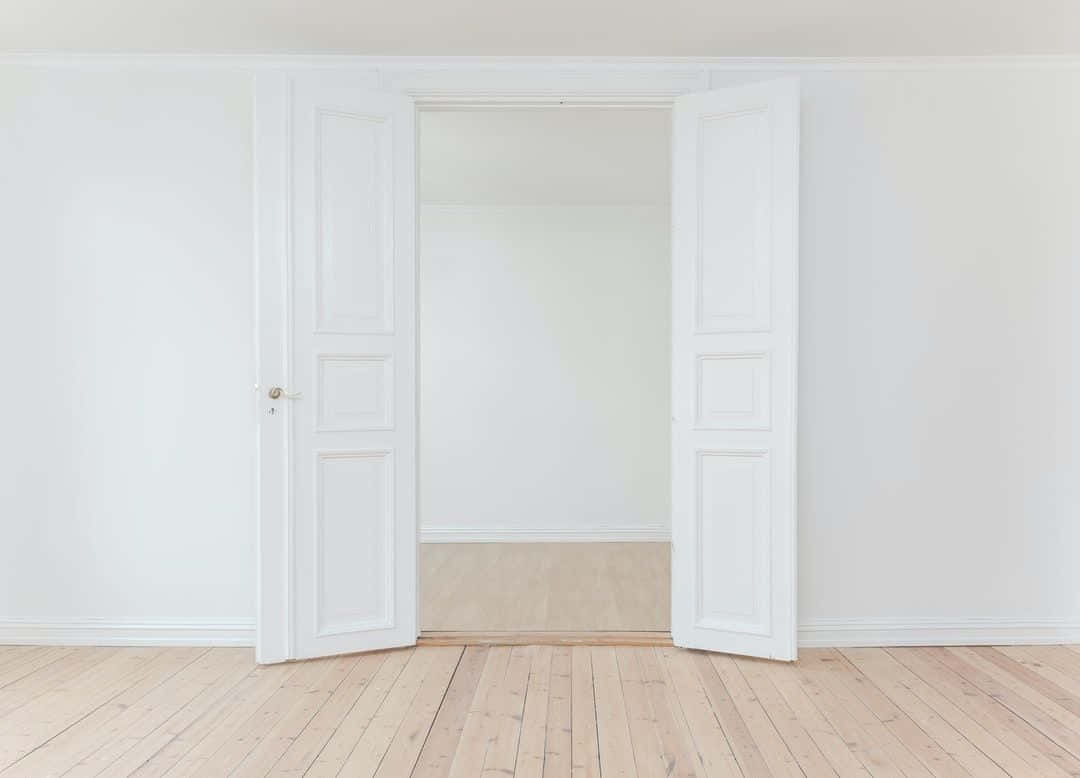Door 桌布 壁紙 — 兩扇白色鑲板門在一個簡約風格的房間中敞開，房間鋪有淺色木地板和純白牆壁。