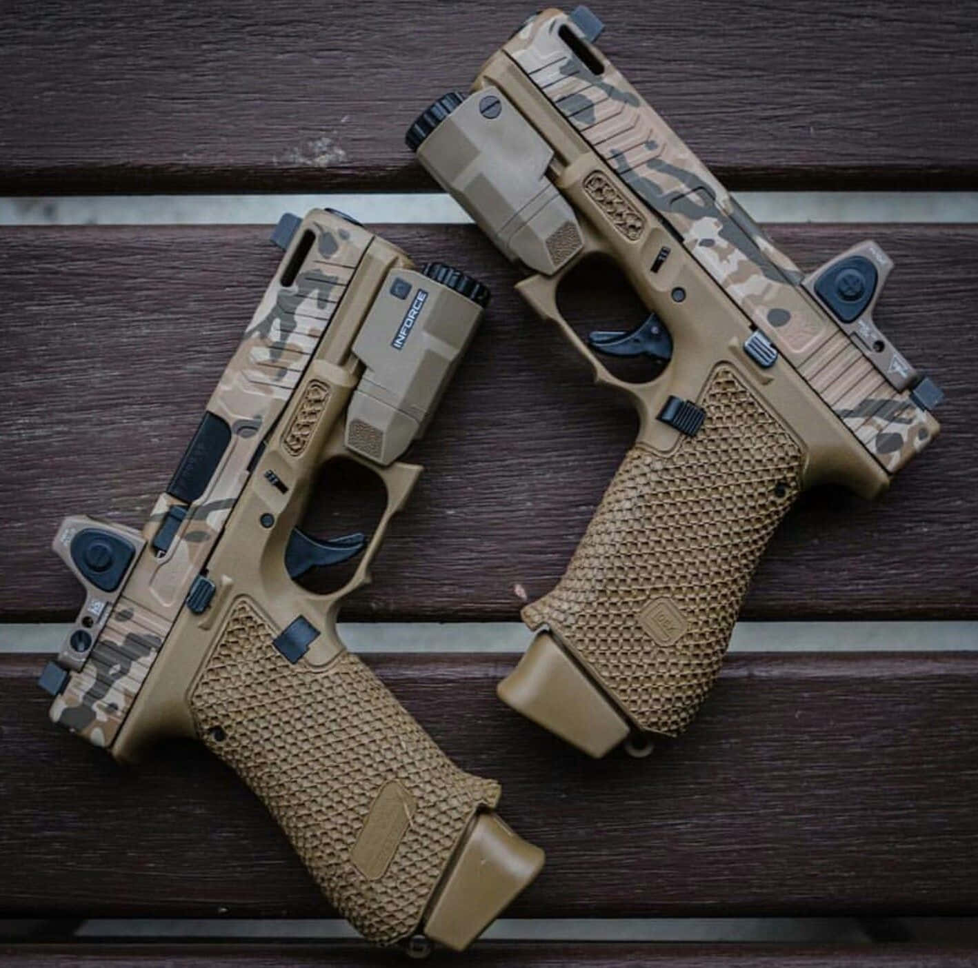 pistol 桌布 壁紙 — 兩把帶有沙漠迷彩握把的戰術手槍以俯視角度放置在深色木條上。