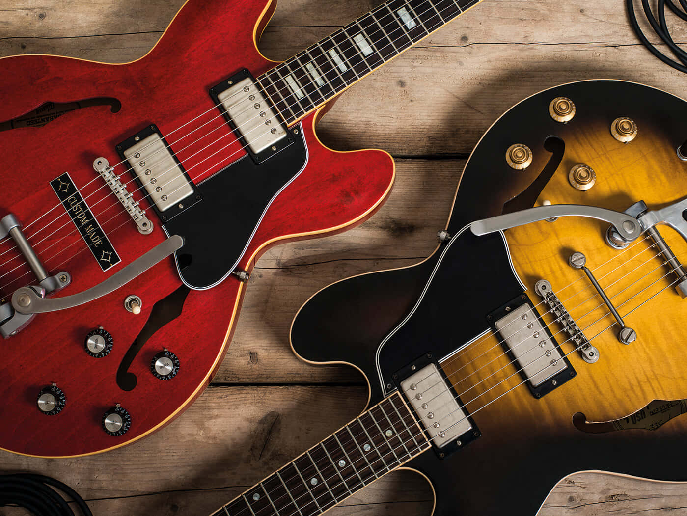 Guitar Aesthetic 桌布 壁紙 — 兩把復古電吉他，一把紅色，一把漸變色，放在溫暖光線下的舊木表面上。