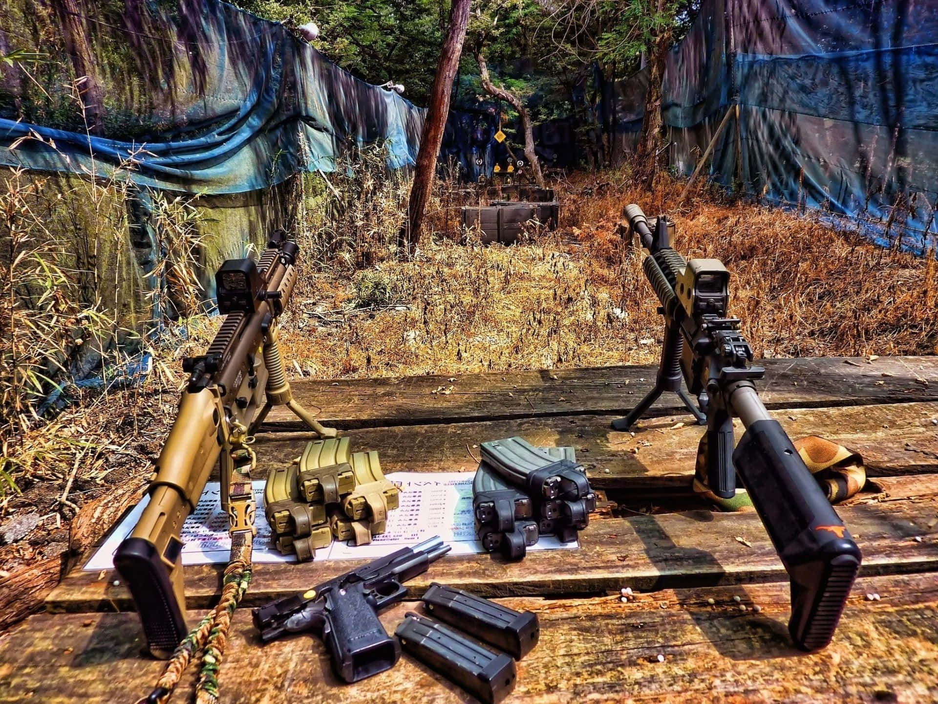 Shooting 桌布 壁紙 — 兩把戰術步槍和手槍連同彈匣放在一張風化的木桌上，位於一個陽光明媚的戶外射擊場，周圍是乾草和藍色防水布。