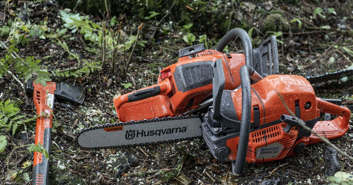 工具 桌布 壁紙 — 兩把橙色Husqvarna電鋸和一把斧頭濕漉漉地躺在森林地面上，周圍是綠色樹葉和落葉。