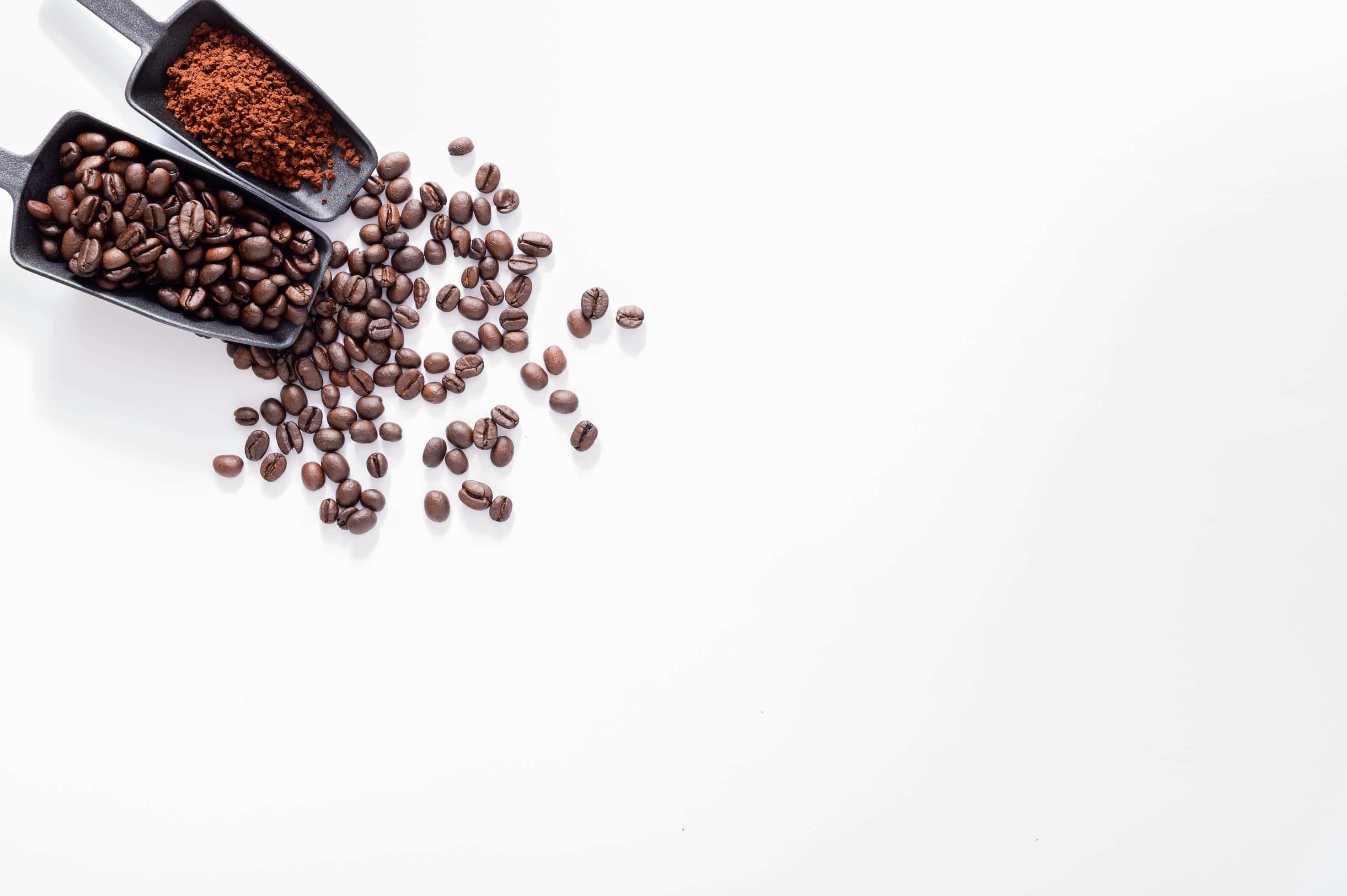 Coffee Beans 桌布 壁紙 — 兩把黑色勺子將完整和研磨的咖啡豆灑在純白表面上，構成極簡主義的畫面。