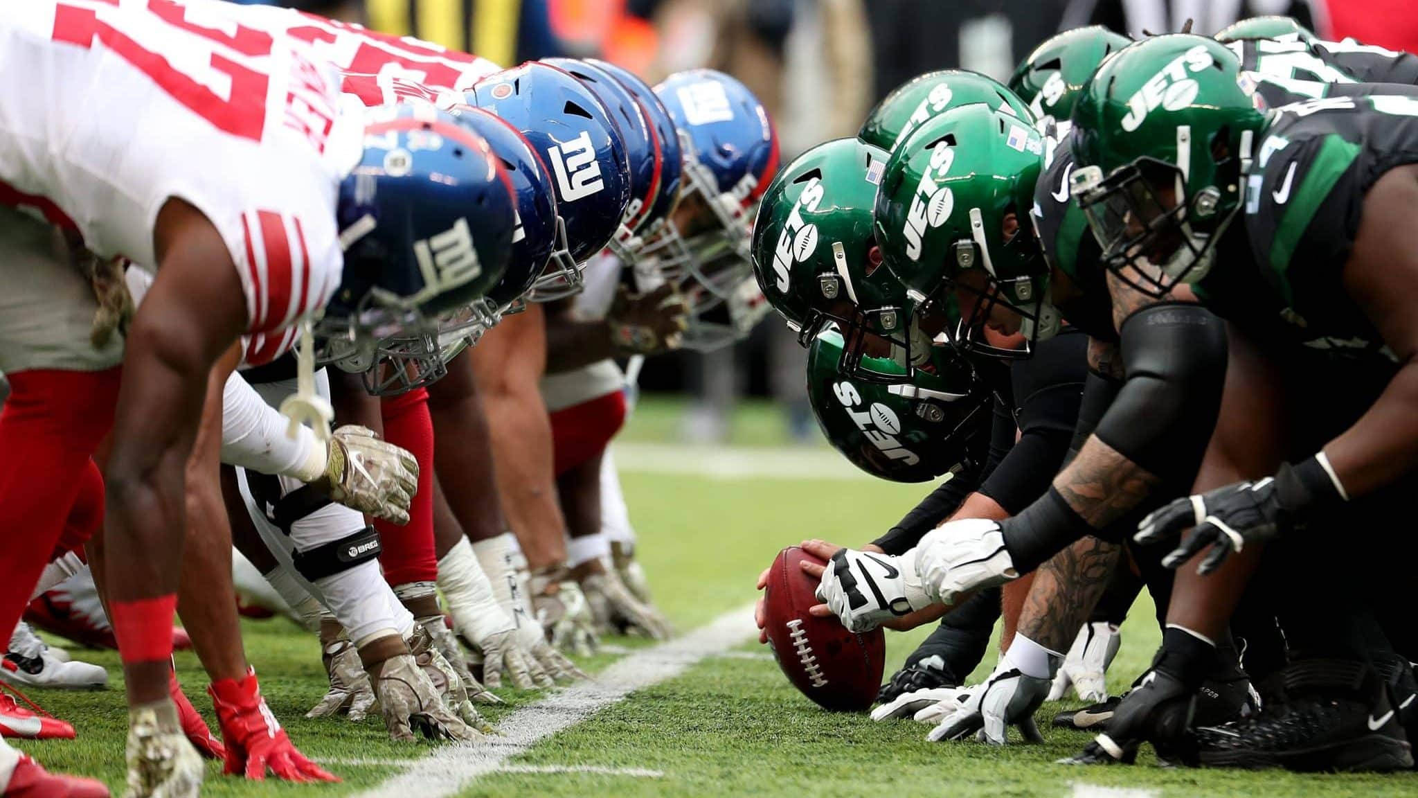 Ny Jets 桌布 壁紙 — 兩支NFL球隊在爭球線以緊張陣式蹲伏，美式足球置於他們之間中央。