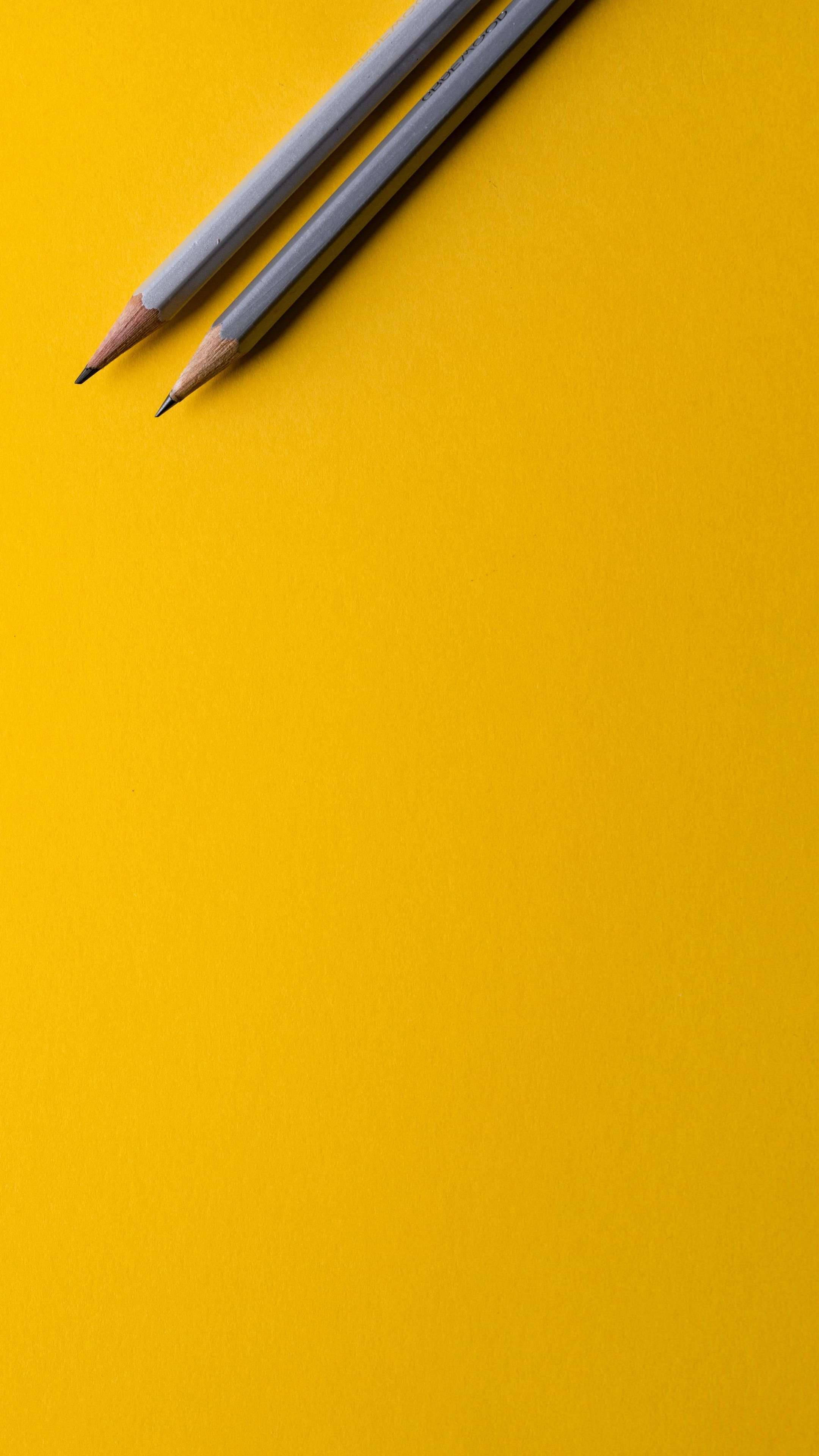 Minimalist Phone 桌布 壁紙 — 兩支削尖的灰色鉛筆對角線地放在充滿活力的黃色紋理背景上。
