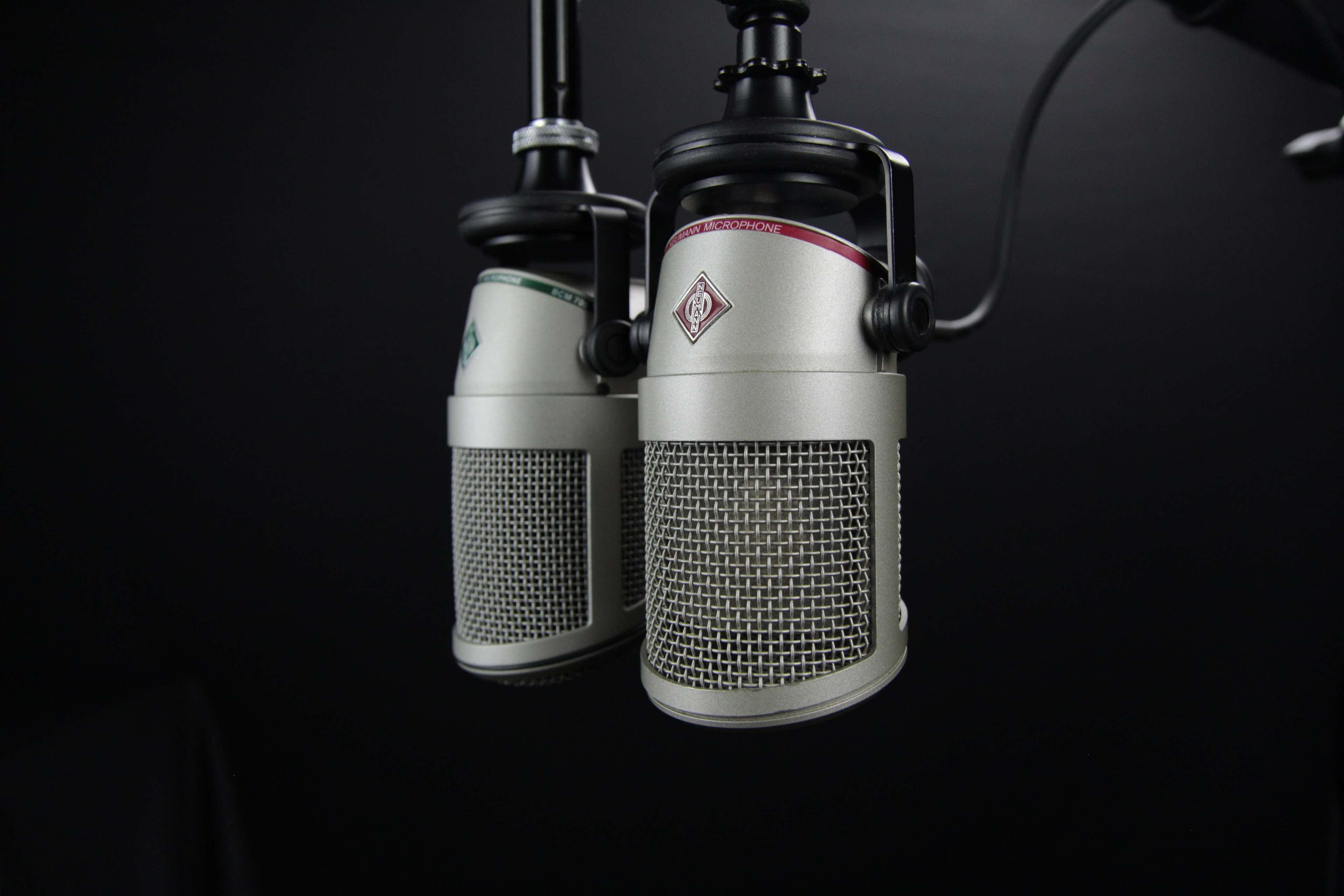 Microphones 桌布 壁紙 — 兩支復古銀色電容麥克風懸掛在簡潔的黑色背景上，帶有戲劇性的燈光效果。