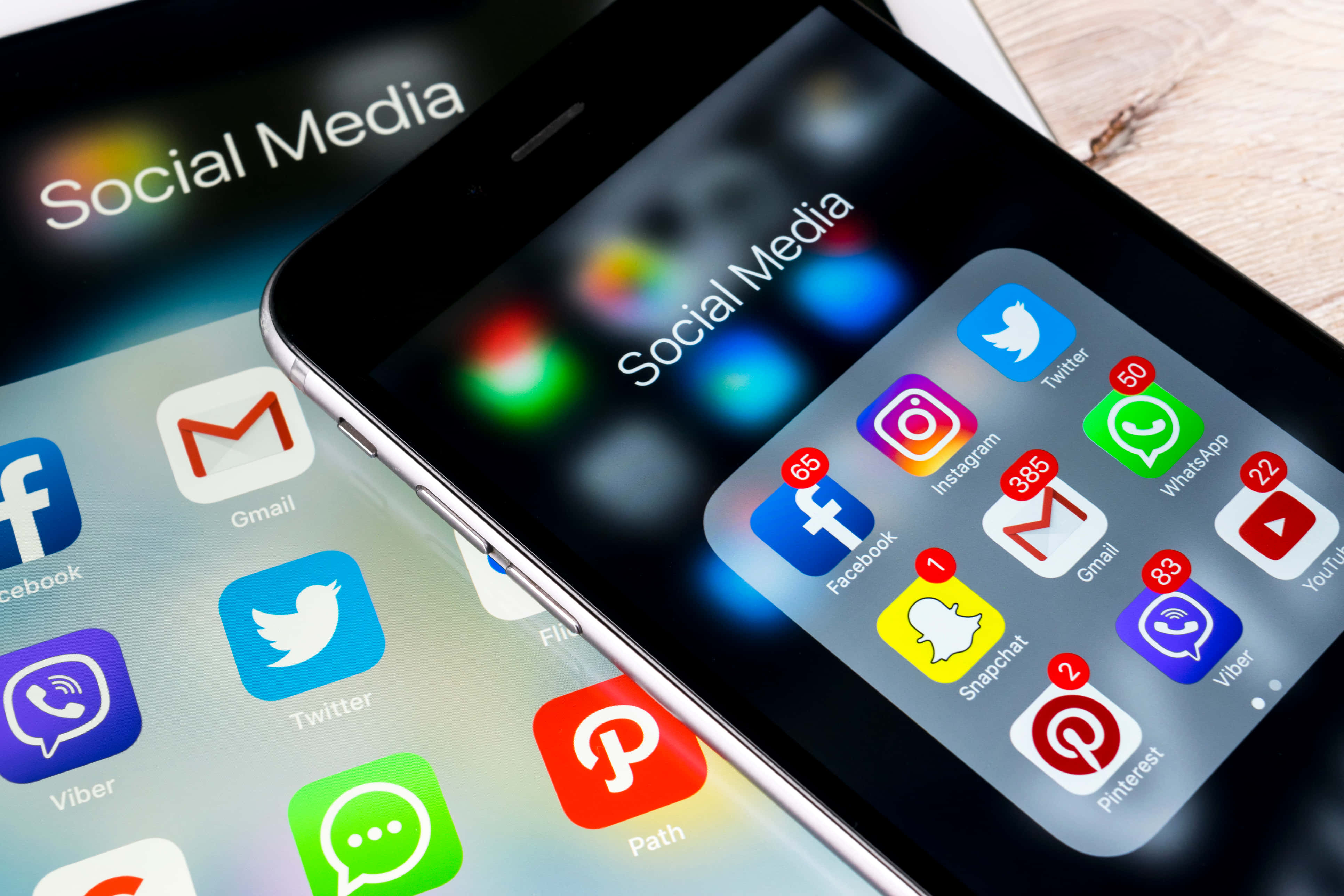 Social Media 桌布 壁紙 — 兩支智慧型手機在木質表面上顯示帶有通知徽章的社交媒體應用程式圖示。