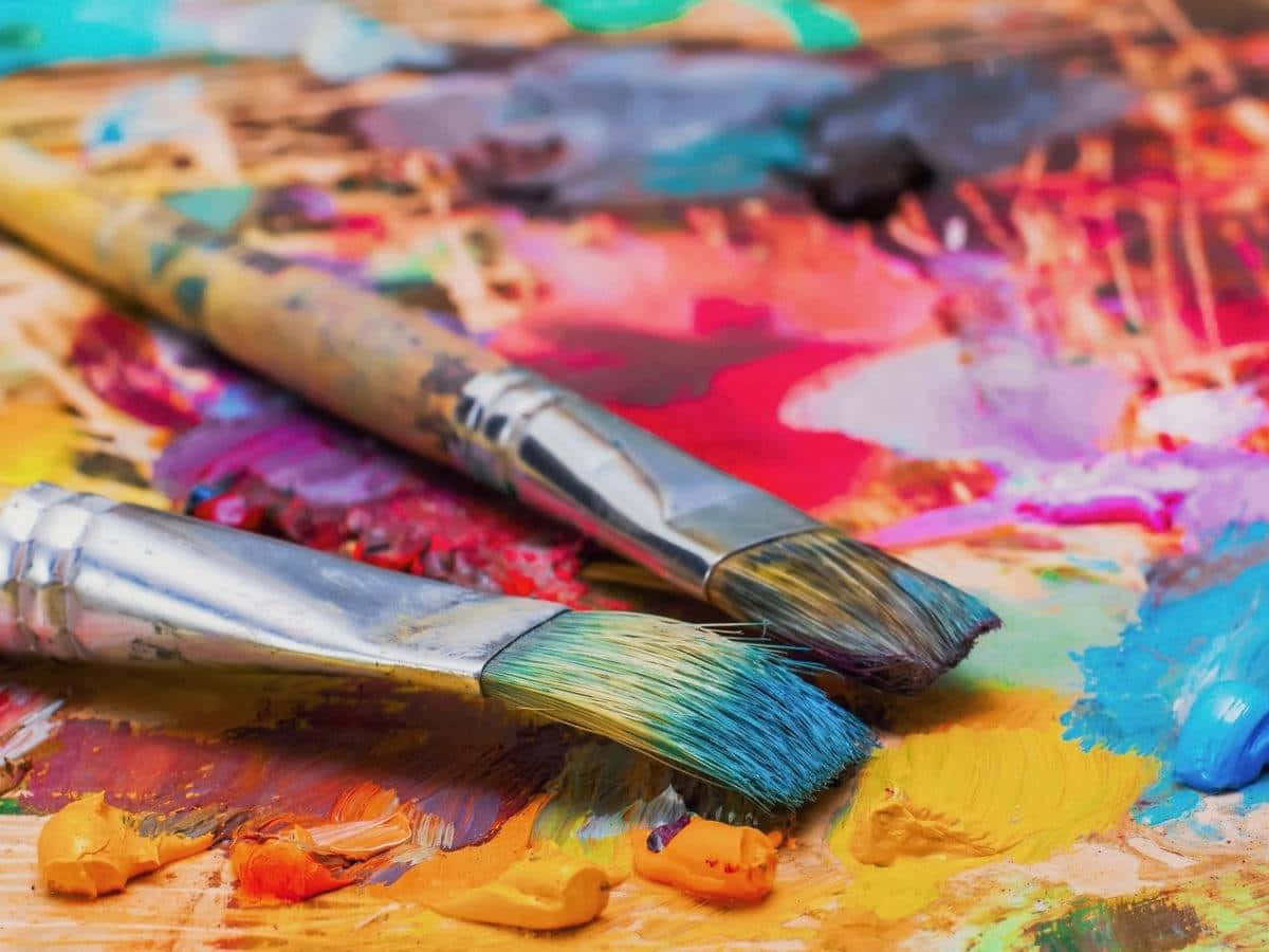 Paint Brush 桌布 壁紙 — 兩支畫筆放在一個充滿活力、有紋理的藝術家調色板上，上面塗滿了大膽混合的顏色。