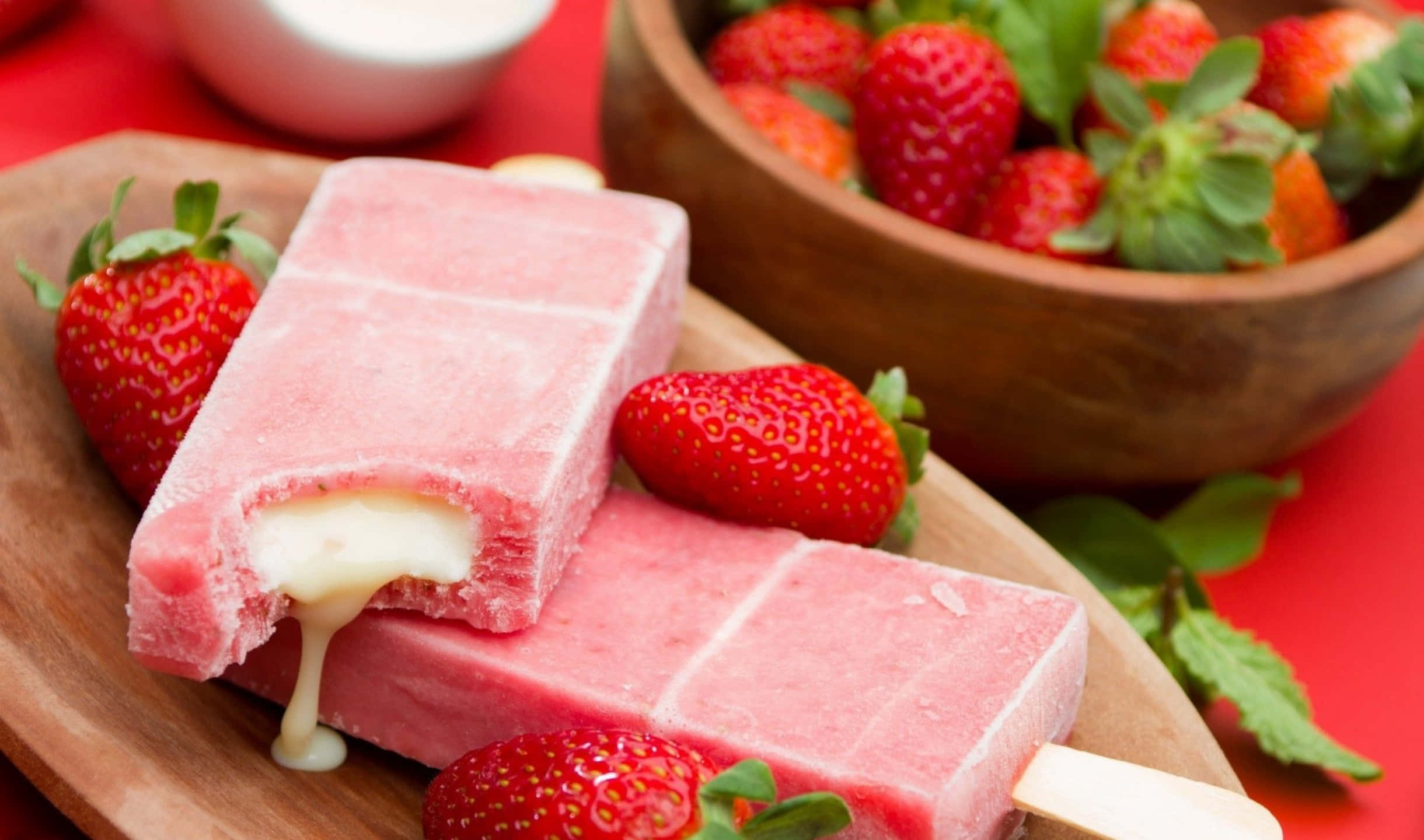 2440x1440 Desserts 桌布 壁紙 — 兩支草莓口味冰棒，中間有融化的奶油內餡，放在木板上，旁邊有新鮮草莓和薄荷葉。