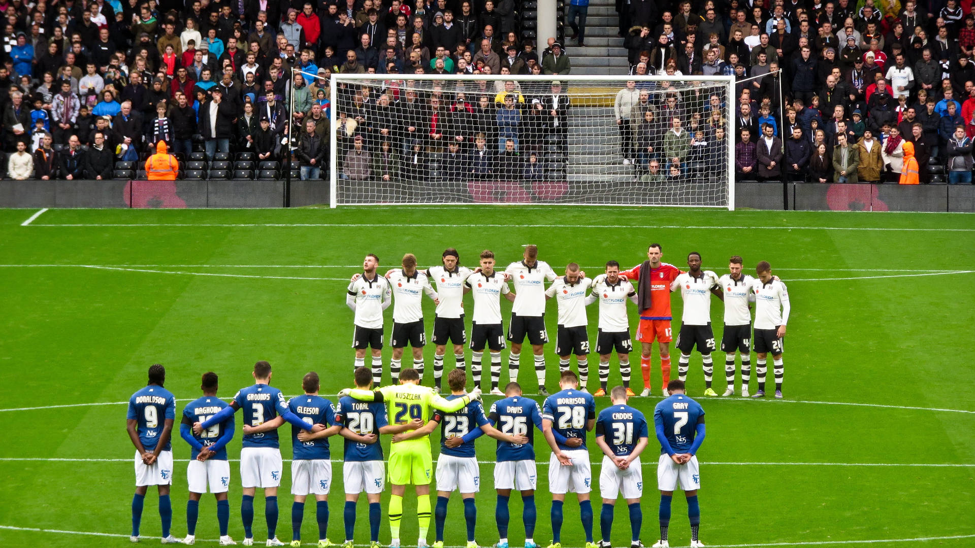 Football Players 桌布 壁紙 — 兩支足球隊在充滿活力的綠色球場上排隊面對面，身後是座無虛席的體育場。