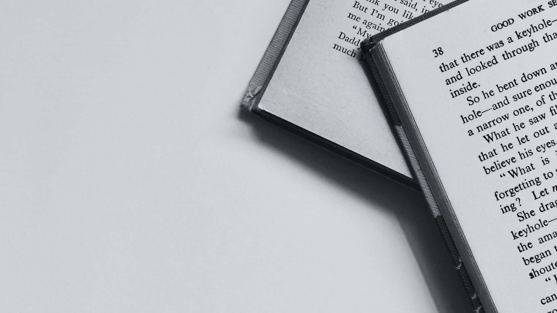 Black And White Book 桌布 壁紙 — 兩本打開的書本，帶有可見的文字，以對角線方式放在純白色表面上，呈現單色調。