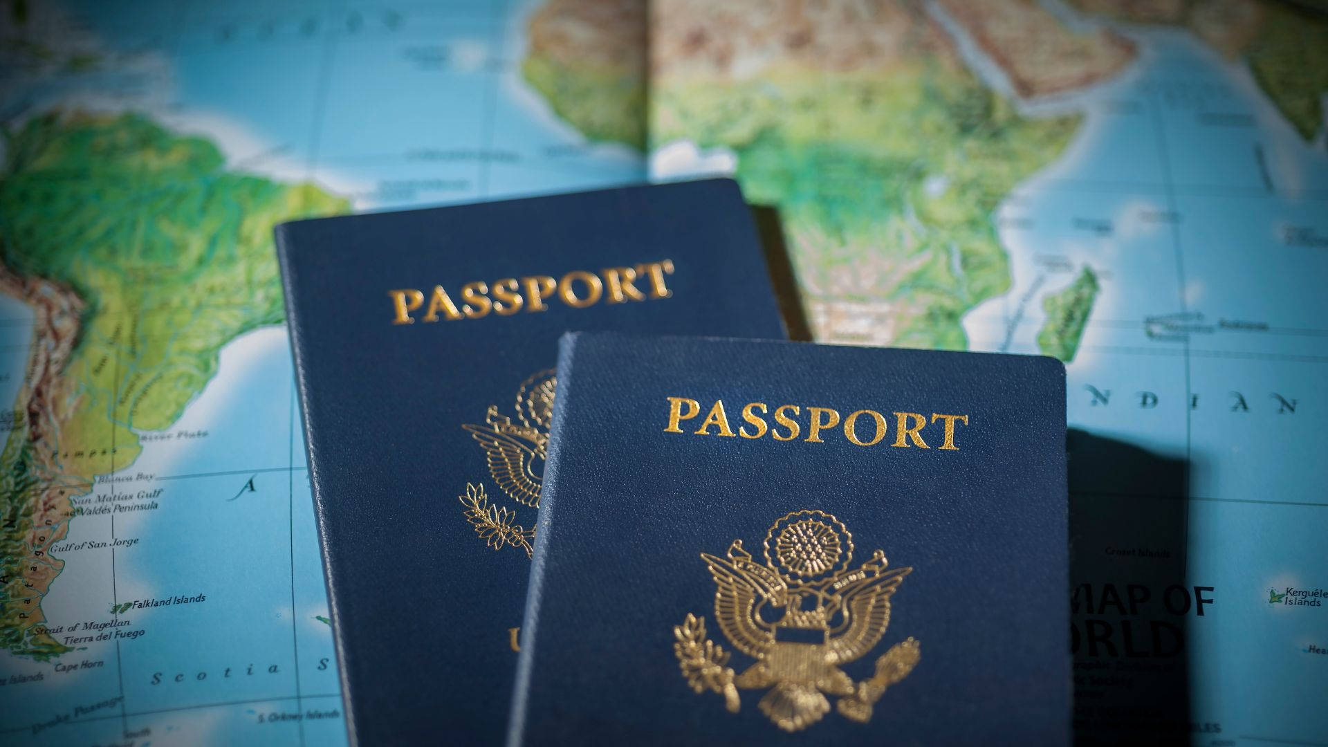 Passport 桌布 壁紙 — 兩本藍色美國護照放在世界地圖上，突顯旅行和國際旅程。