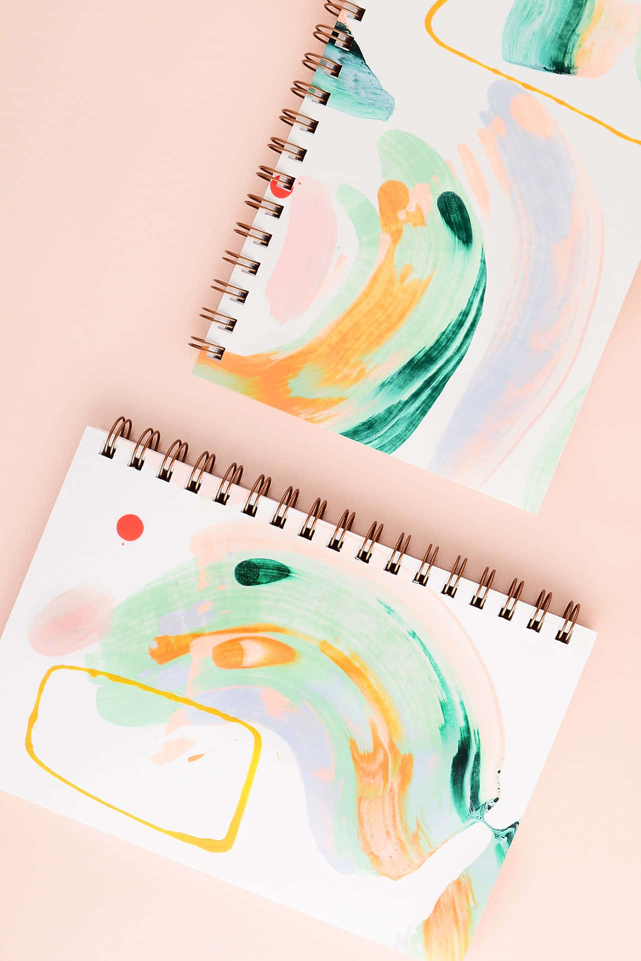 Notebook 桌布 壁紙 — 兩本螺旋筆記本，帶有青綠色、橙色和粉紅色的抽象水彩漩渦，放置在柔和的蜜桃色背景上。
