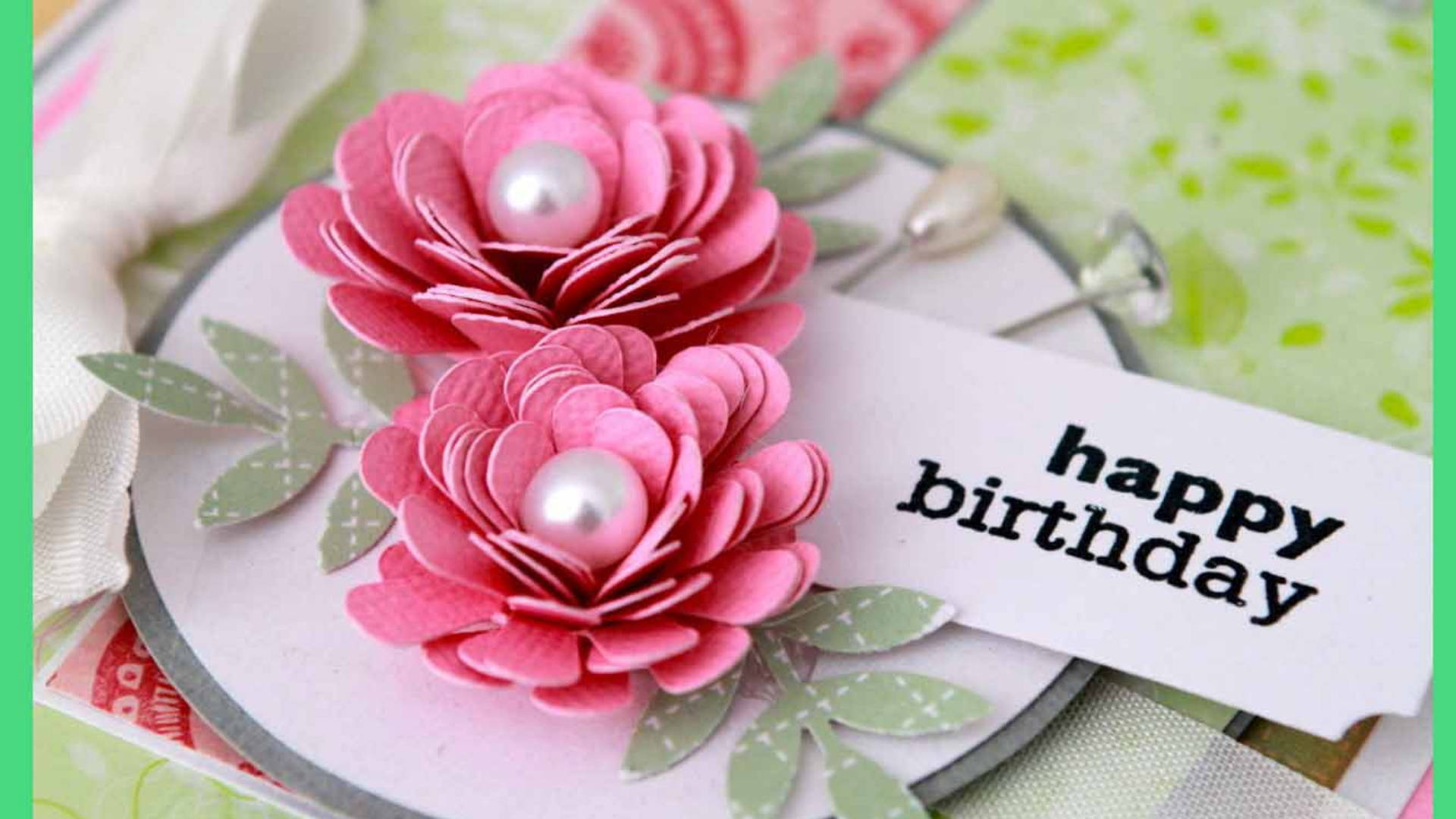 Happy Birthday Flower 桌布 壁紙 — 兩朵精緻分層的粉紅色紙花，帶有珍珠花心，點綴著一張被圖案紙和絲帶環繞的生日卡。