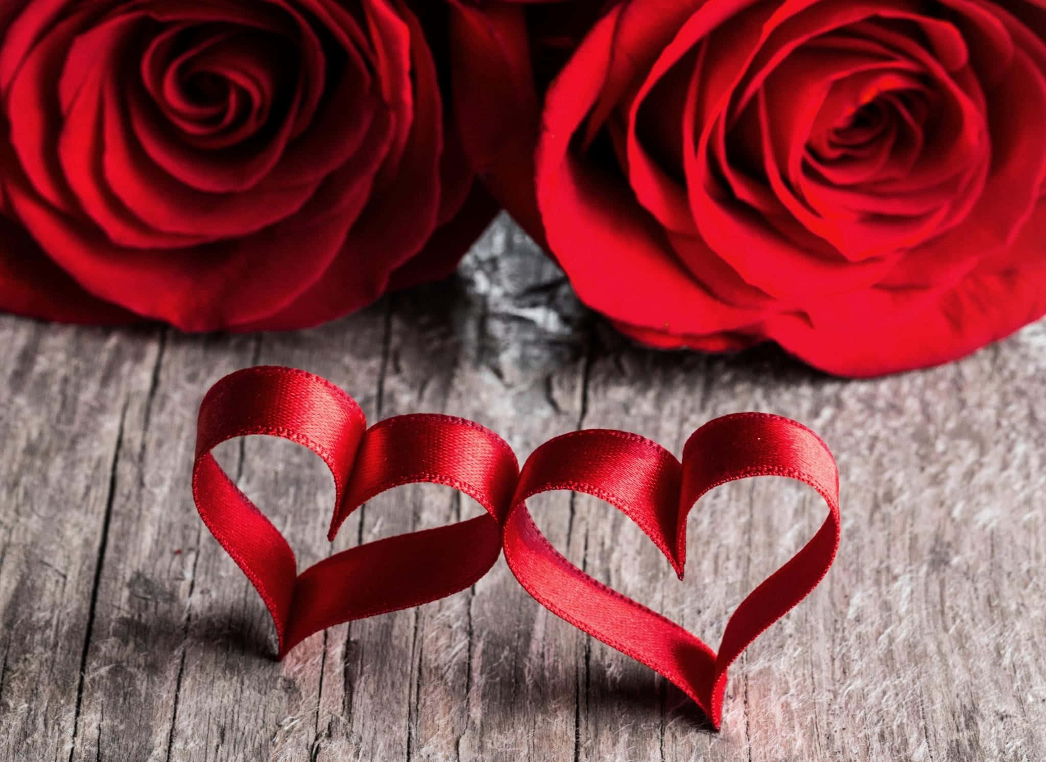 Rose Heart 桌布 壁紙 — 兩朵鮮豔的紅玫瑰和兩個紅色絲帶心形放在風化的木質表面上。