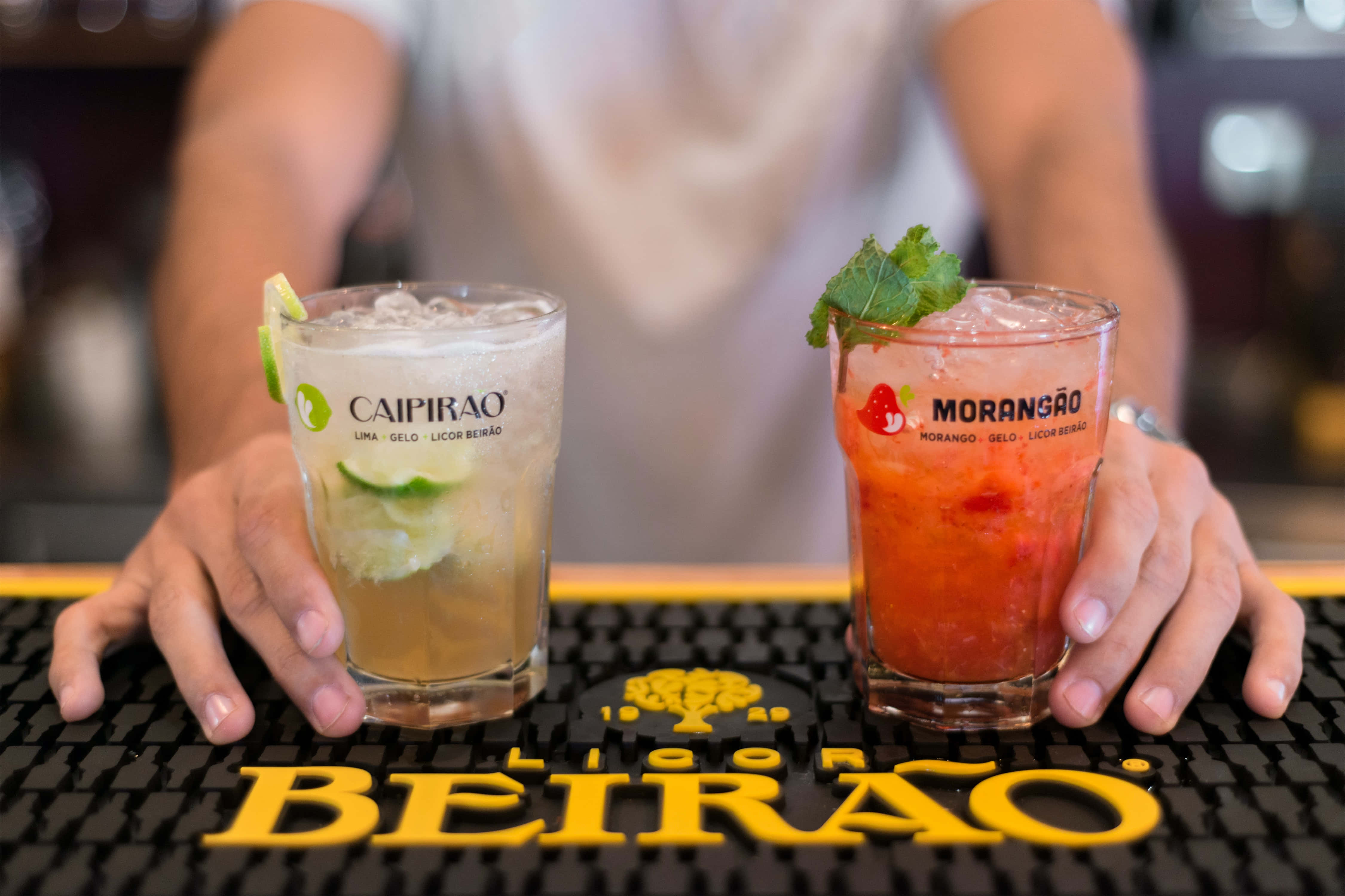 Summer Drinks 桌布 壁紙 — 兩杯充滿活力的巴西雞尾酒，配上萊姆和薄荷裝飾，放在吧檯墊上，由調酒師呈上。