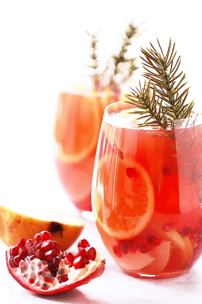 Winter Drinks 桌布 壁紙 — 兩杯充滿活力的紅石榴和柑橘飲料，飾以迷迭香枝和橙片。