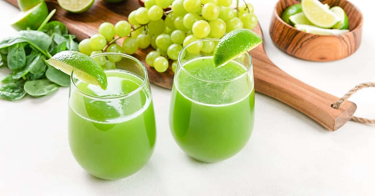 兩杯綠色果汁配以萊姆裝飾，周圍是新鮮葡萄和菠菜。 — Juice Wrld 壁紙