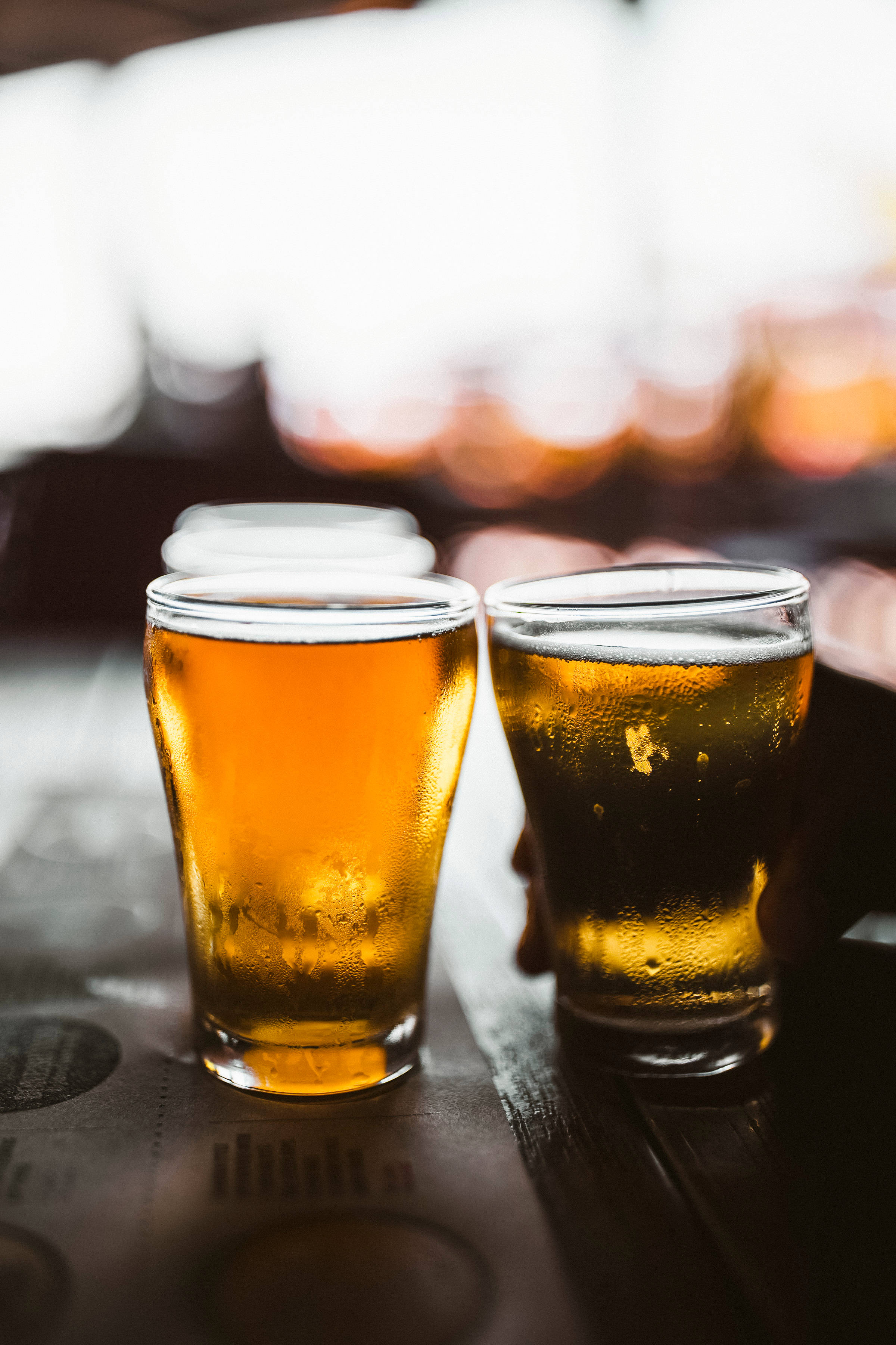 Beer 桌布 壁紙 — 兩杯冰凍琥珀色啤酒杯在深色木吧檯上閃爍著冷凝水珠，背後有柔和散景燈光。