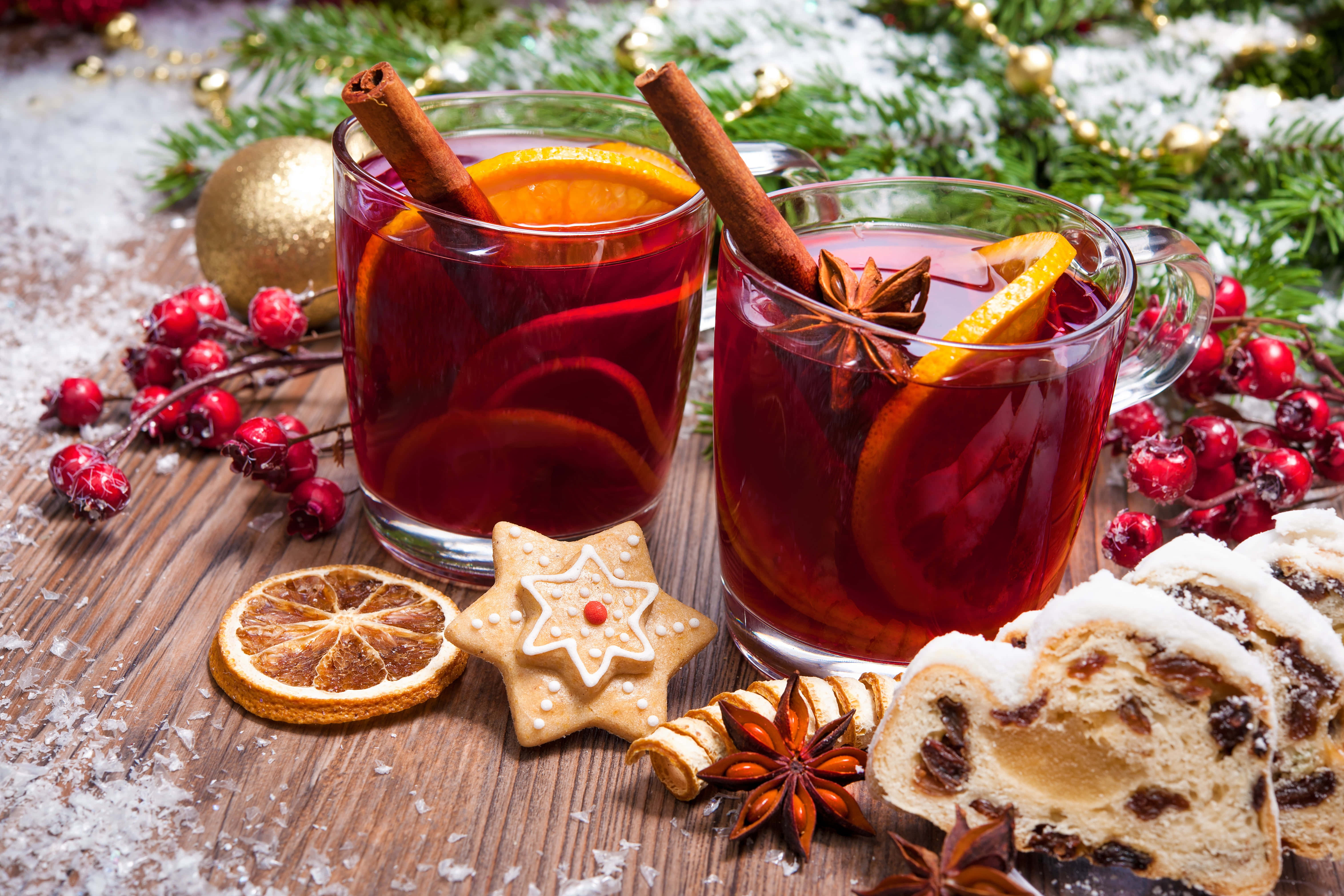 Mulled Wine 桌布 壁紙 — 兩杯加了肉桂棒和橙片的香料熱紅酒，旁邊放著節日薑餅曲奇和切片聖誕麵包，置於鋪雪的木桌上。