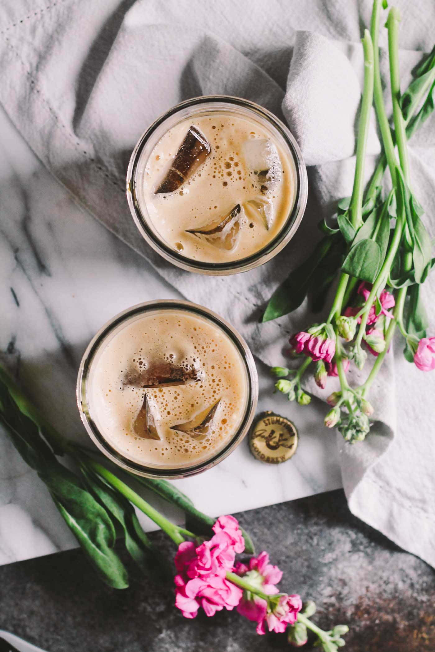 Iced Coffee 桌布 壁紙 — 兩杯加冰塊和巧克力片的冰咖啡放在大理石表面上，旁邊有粉紅色的花和一塊布。