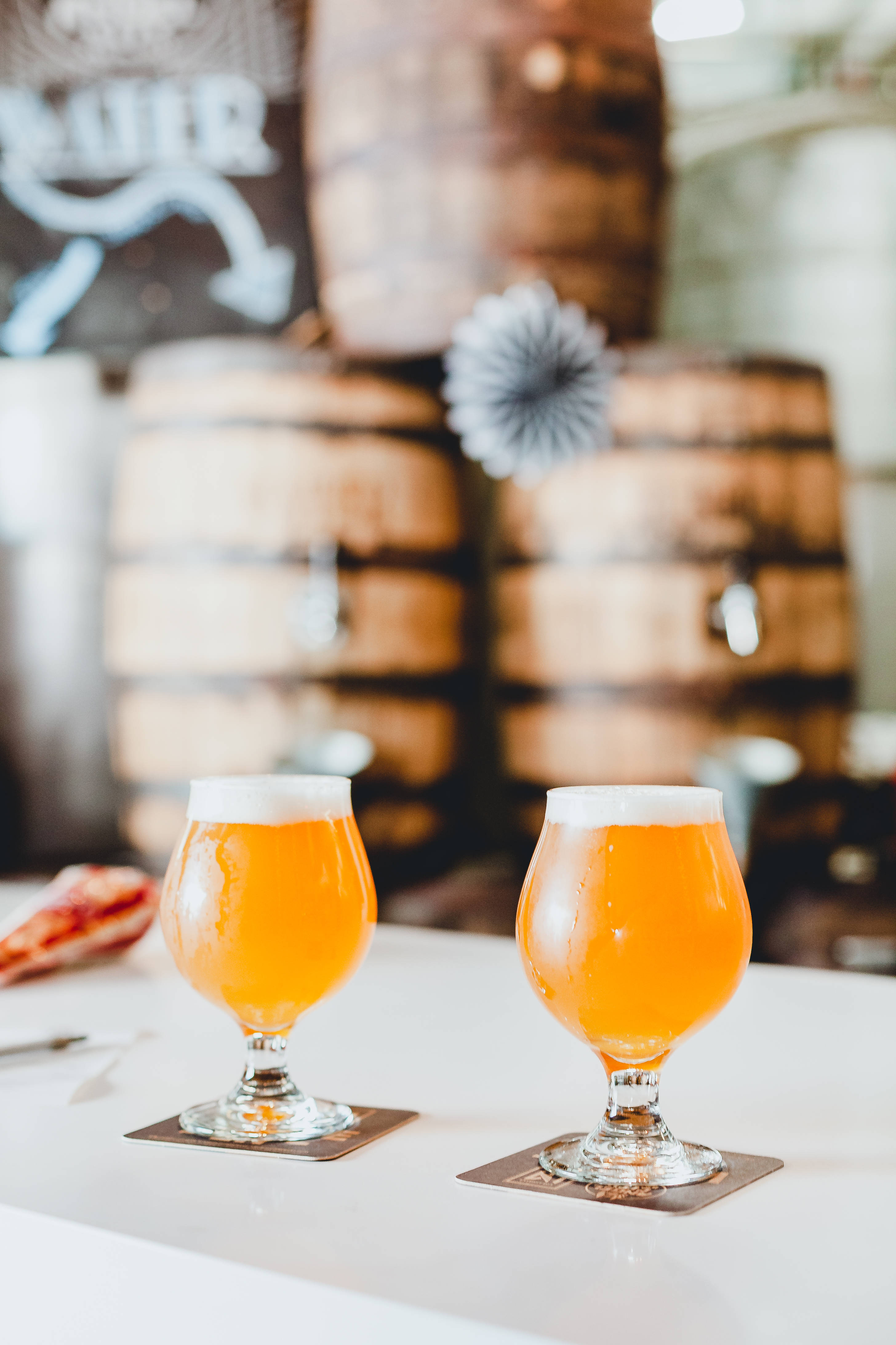 Beer 桌布 壁紙 — 兩杯泡沫豐富的琥珀色啤酒放在鬱金香杯中，置於杯墊上，背景是釀酒廠的木桶。