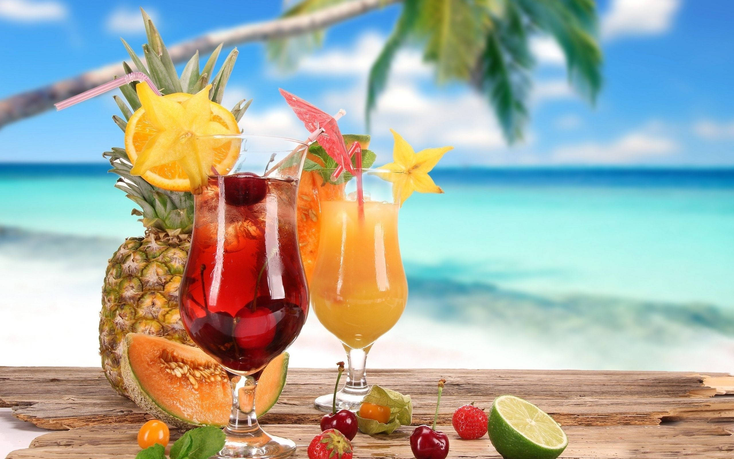 Drink 桌布 壁紙 — 兩杯熱帶雞尾酒，飾以水果和海星，放在木桌上，背景是充滿活力的海灘。