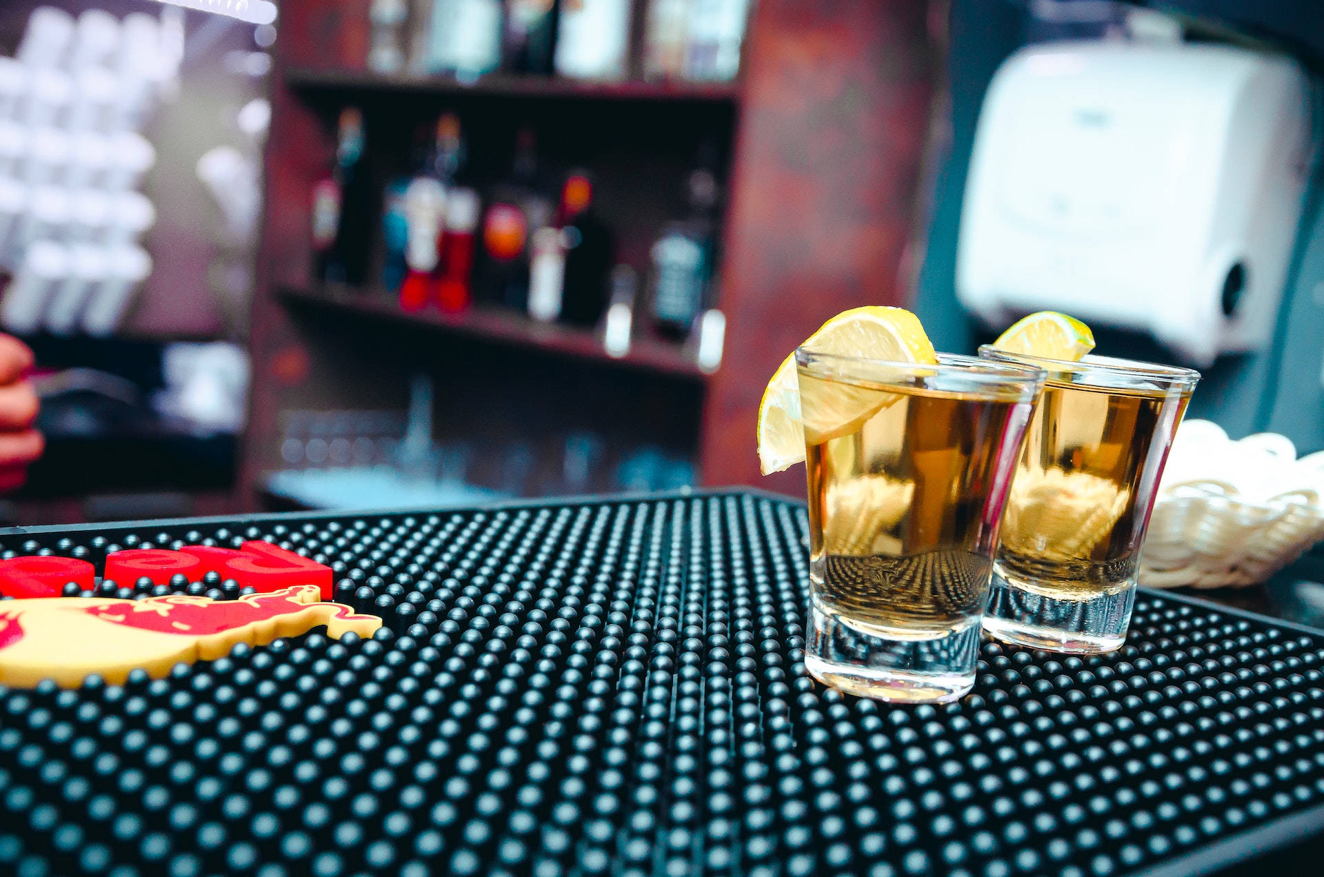 alcohol 桌布 壁紙 — 兩杯琥珀色烈酒飾以檸檬角，放在黑色吧檯墊上，旁邊有一個紅黃色杯墊。