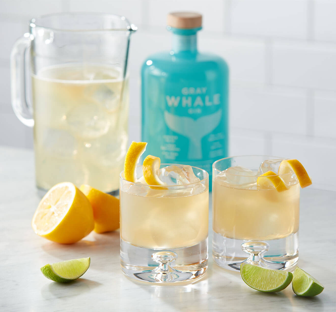 alcohol 桌布 壁紙 — 兩杯琴酒雞尾酒配以檸檬和萊姆裝飾，放在一個水壺和藍色琴酒瓶旁邊的大理石檯面上。