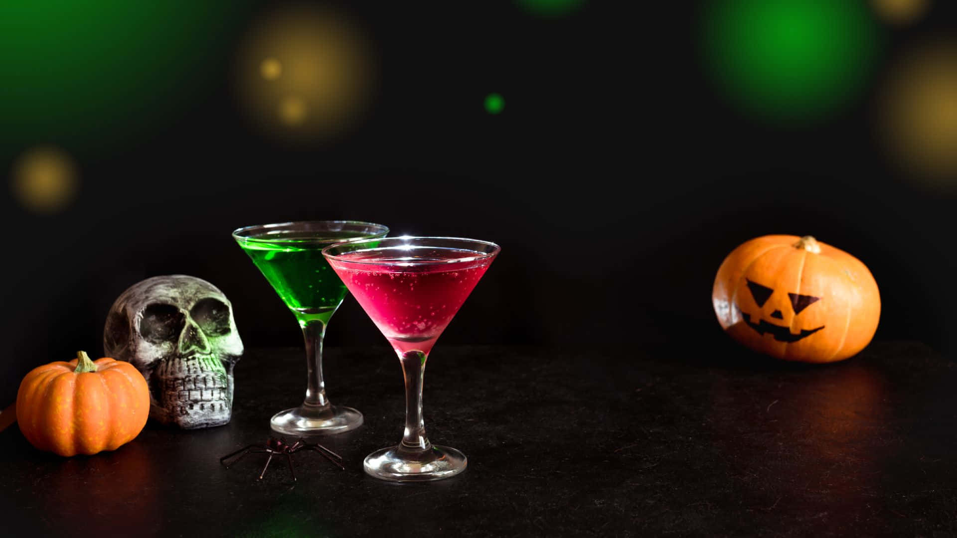 Spooky Cocktails 桌布 壁紙 — 兩杯發光的馬丁尼雞尾酒放在南瓜和骷髏旁邊，置於帶有綠色散景燈光的暗色桌子上。