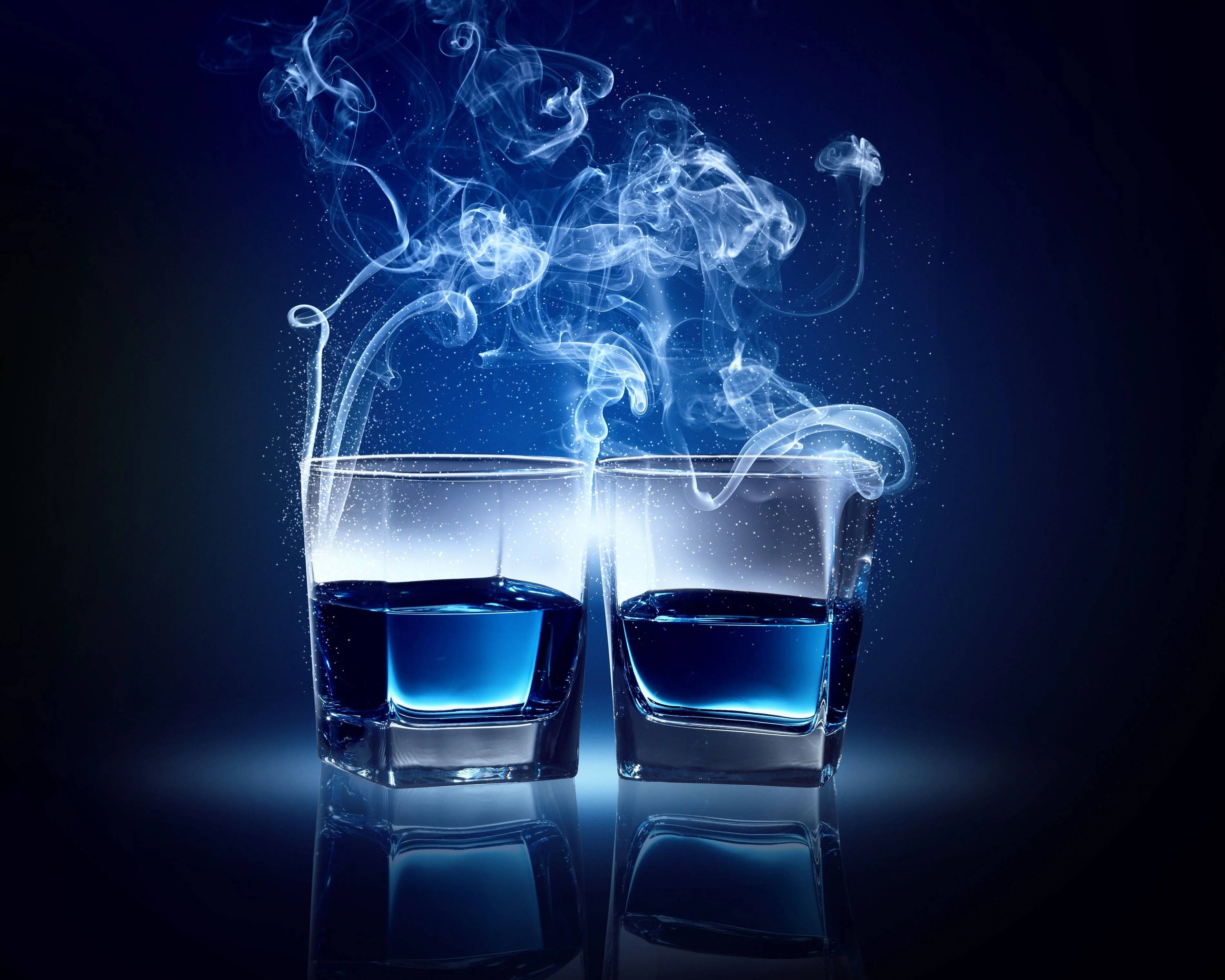 Drink 桌布 壁紙 — 兩杯發光藍色液體在黑暗背景及反射表面上散發出旋轉煙霧。