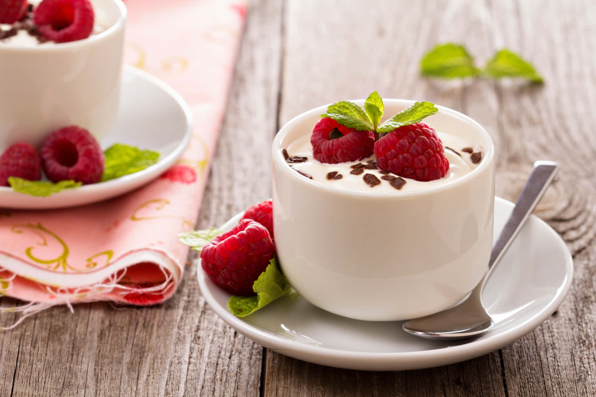 Cute Dessert 桌布 壁紙 — 兩杯白色奶油甜點，上面鋪上新鮮覆盆子、薄荷葉和巧克力碎，放在質樸的木桌上。