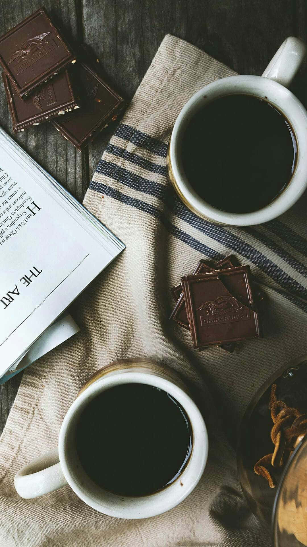 桌布 壁紙 — 兩杯白色馬克杯的黑咖啡放在條紋布上，旁邊有巧克力條和一本打開的書，置於鄉村風木桌上。