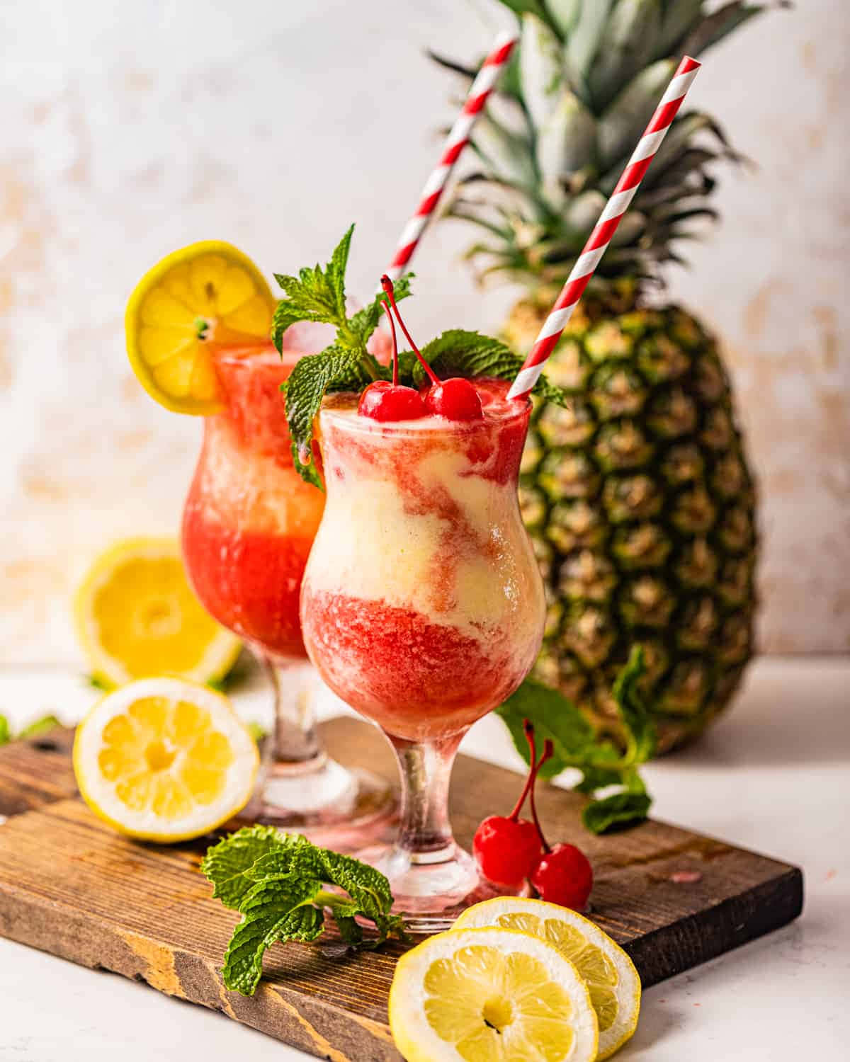 檸檬 桌布 壁紙 — 兩杯色彩鮮豔的熱帶飲品，飾以櫻桃、薄荷和檸檬片，旁邊放著一個完整的鳳梨，置於質樸的木板上。