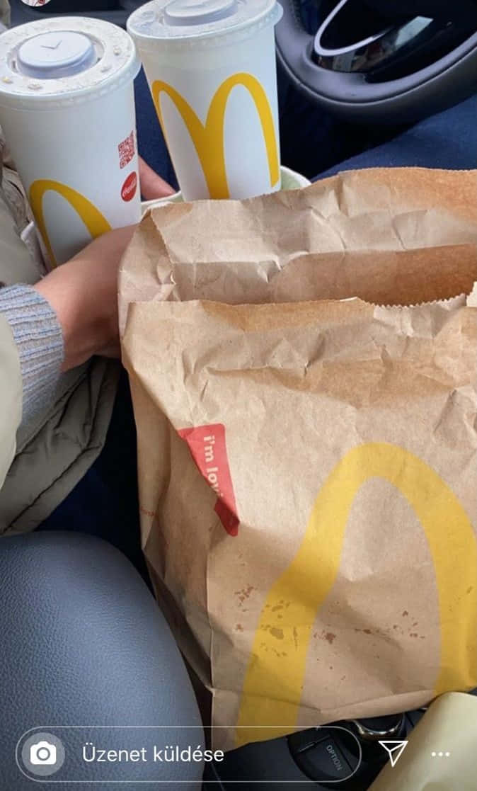 Mcdonalds Food 桌布 壁紙 — 兩杯麥當勞飲料和紙袋放在車內，旁邊有一隻手拿著一個杯子。