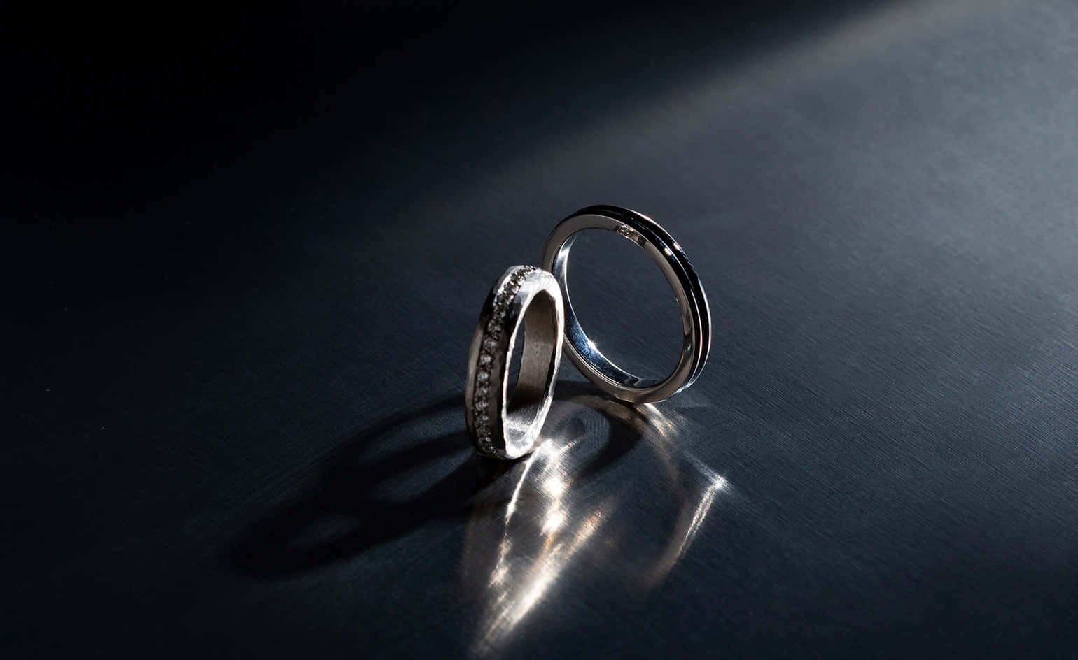 Marriage 桌布 壁紙 — 兩枚優雅的結婚戒指在黑暗反光表面上，於戲劇性的聚光燈下閃耀。