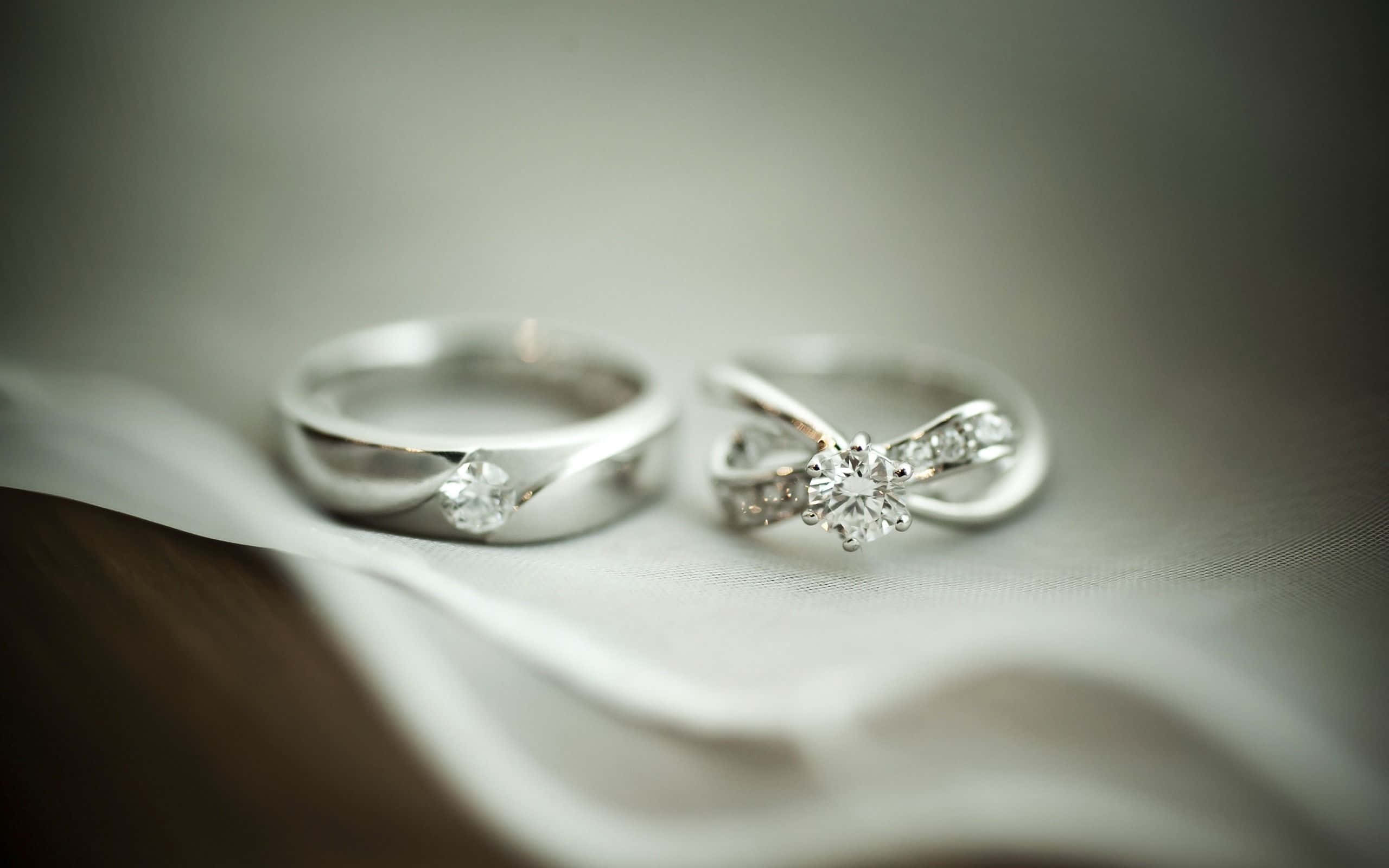 Wedding Rings 桌布 壁紙 — 兩枚優雅的鑽石戒指放在柔軟的白色布料上，景深較淺。