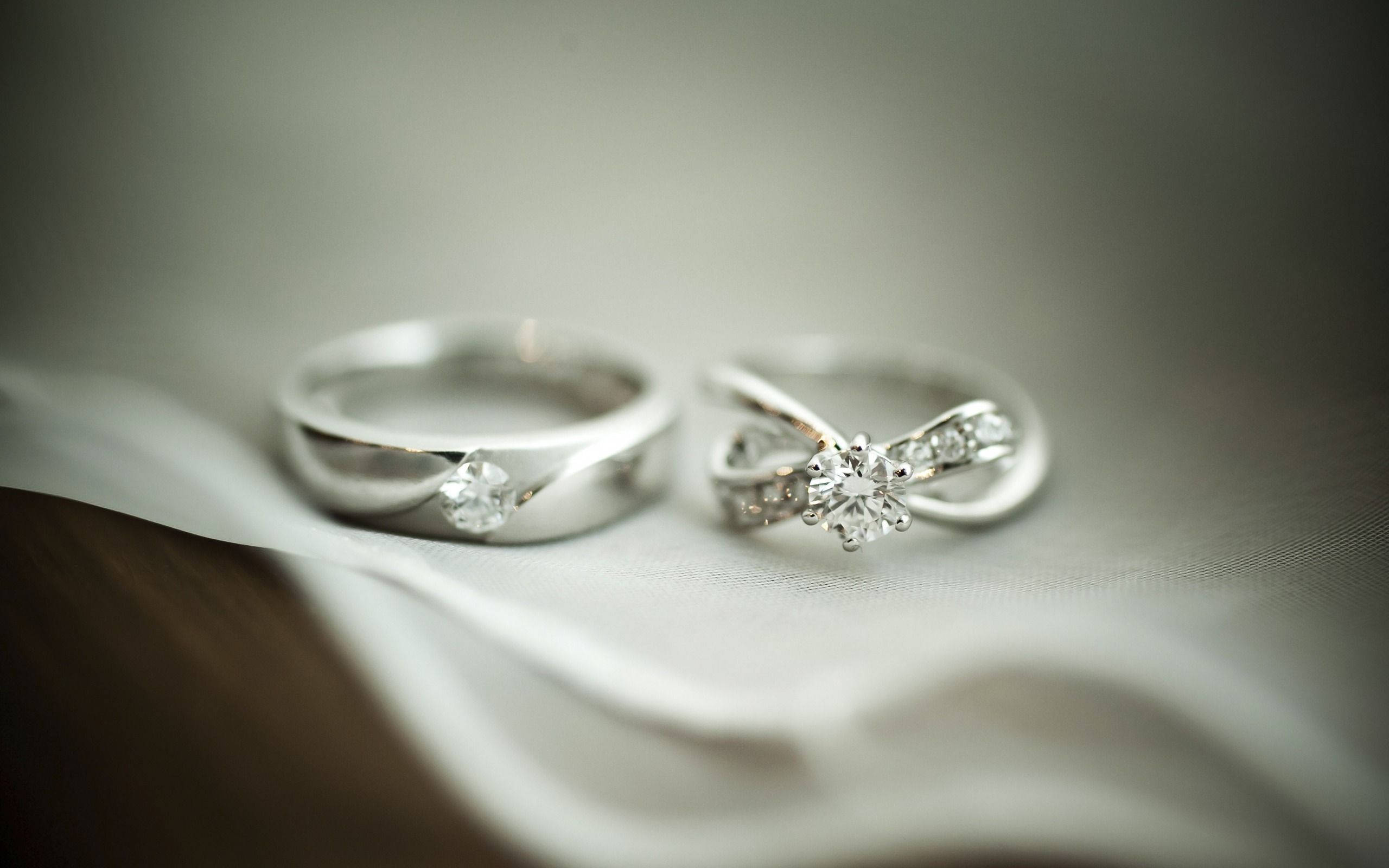 Wedding Rings 桌布 壁紙 — 兩枚優雅的鑽石結婚戒指放在柔軟的白色布料上，景深較淺。
