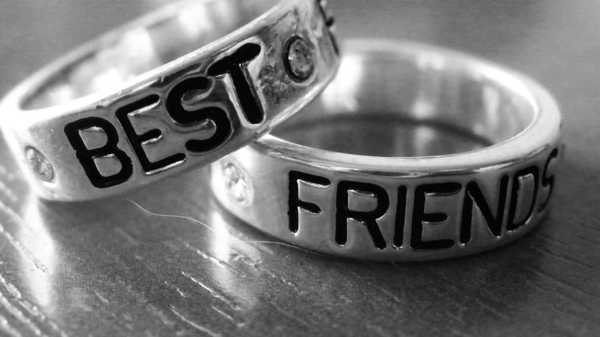 Typography 桌布 壁紙 — 兩枚刻有「BEST FRIENDS」字樣的銀戒指，在單色特寫中放置在木質表面上。