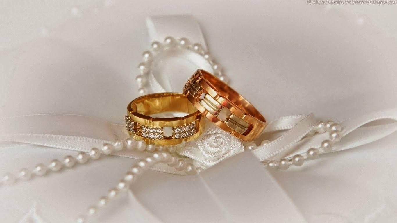 Wedding Rings 桌布 壁紙 — 兩枚帶鑽石的黃金結婚戒指優雅地放置在白色緞帶和珍珠鏈上。