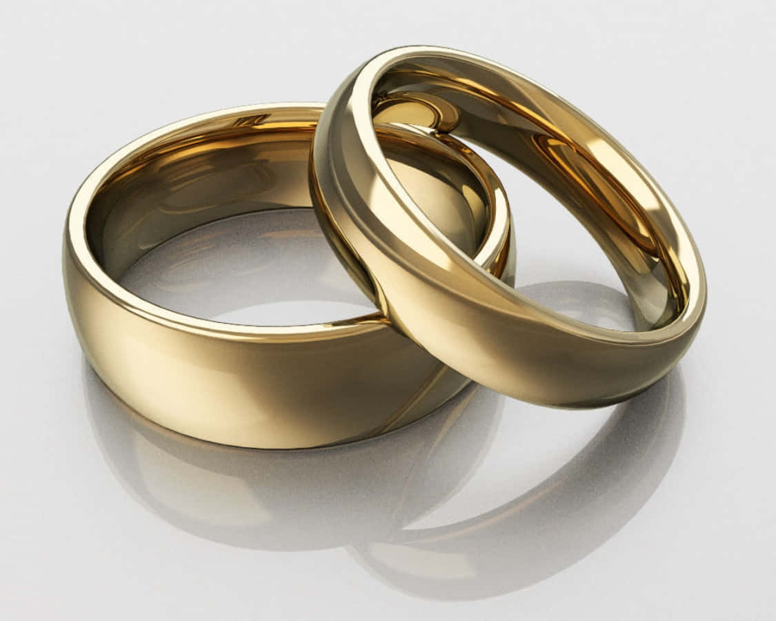Wedding Rings 桌布 壁紙 — 兩枚拋光金色結婚戒指在反光的白色表面上交織，帶有柔和陰影。