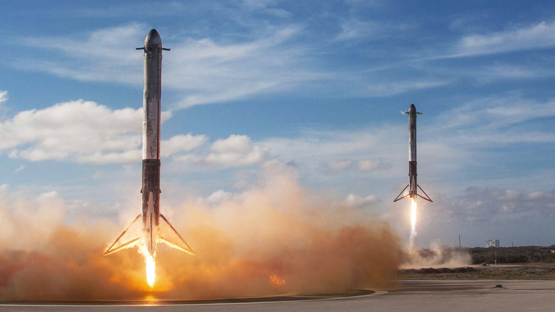 SpaceX 桌布 壁紙 — 兩枚火箭在明亮的藍天和散落的雲朵下，從發射台點燃熾熱的推力升空。