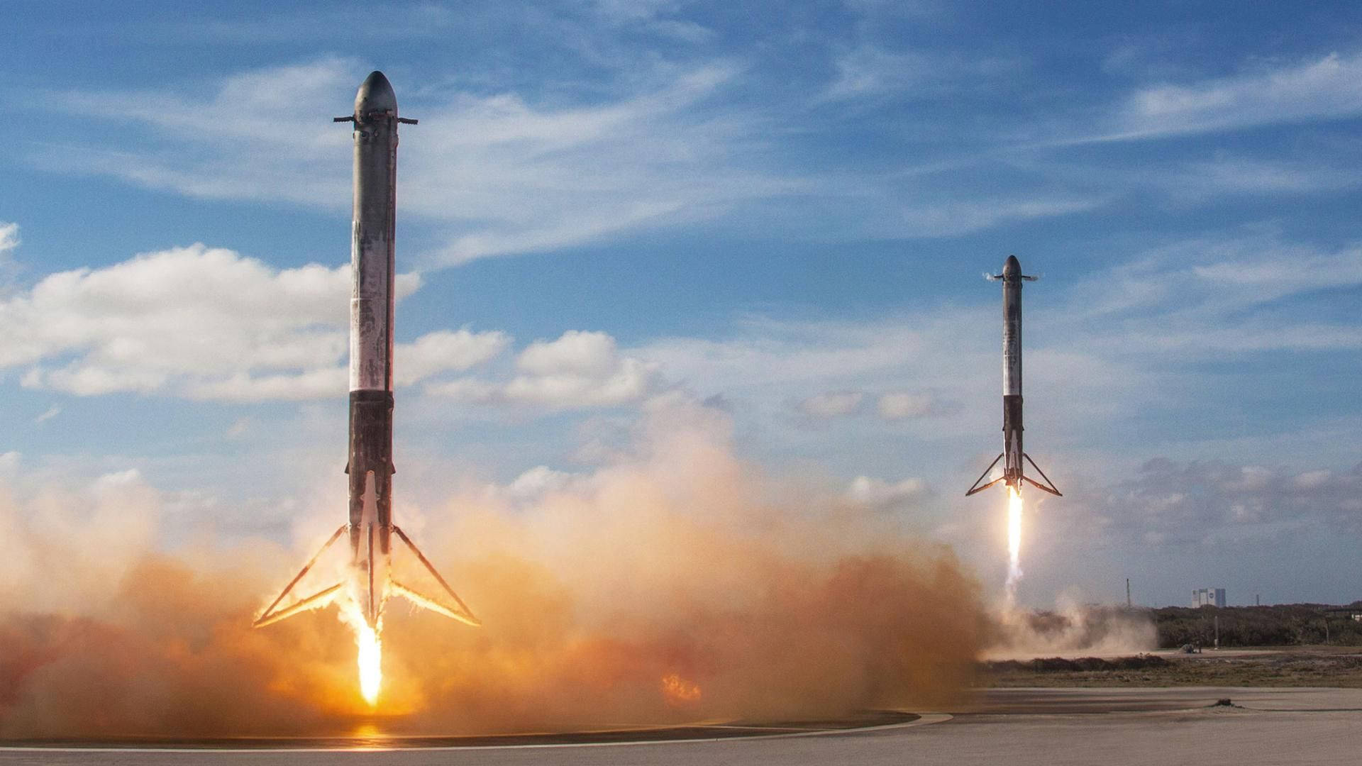SpaceX 桌布 壁紙 — 兩枚火箭在藍天下以熾熱推力點燃，從發射台戲劇性地垂直升空。
