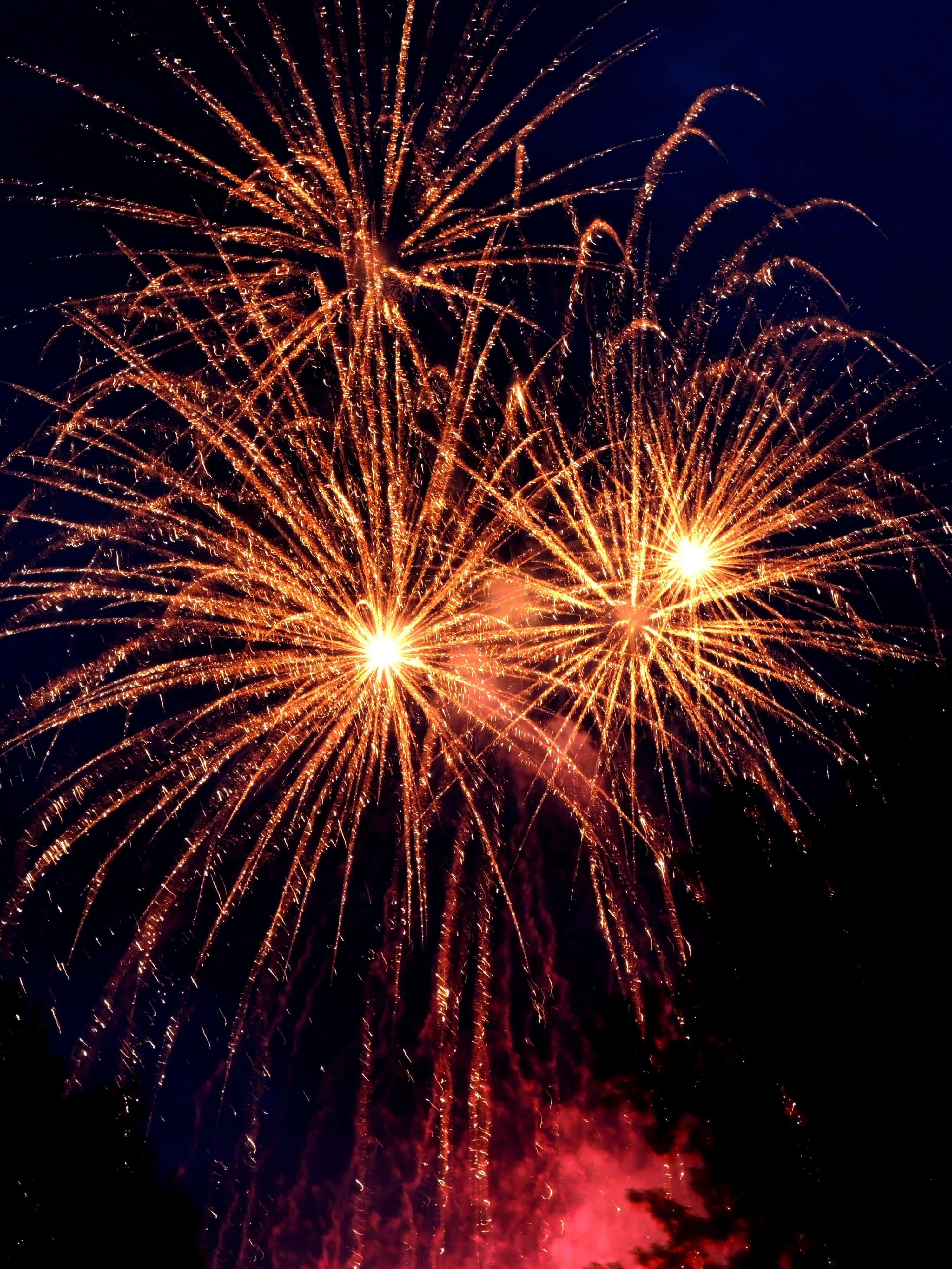 Fireworks 桌布 壁紙 — 兩枚燦爛的金色煙火在黑暗的夜空中爆炸，散發出耀眼火花，下方帶有一絲紅煙。