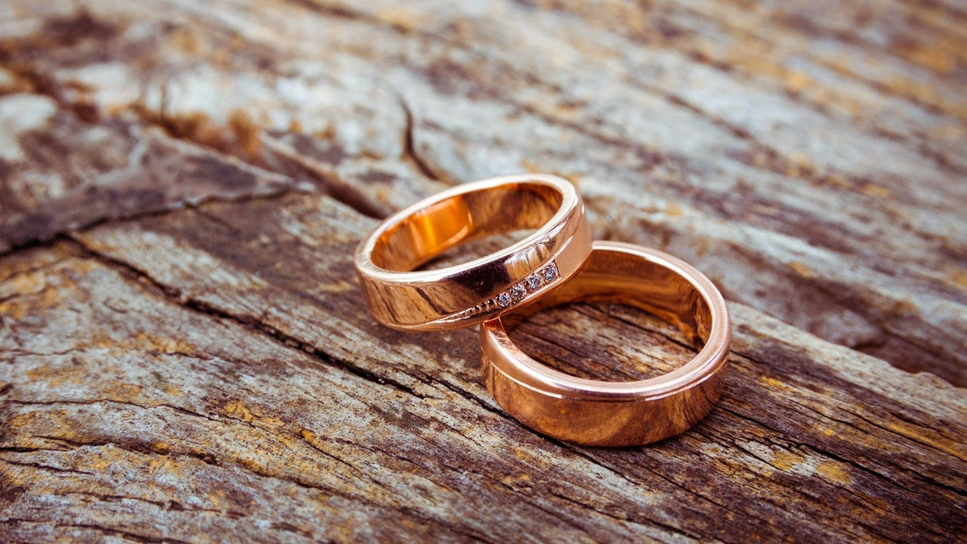 Wedding Rings 桌布 壁紙 — 兩枚玫瑰金結婚戒指帶有鑽石點綴，親密地放在風化的木質表面上。
