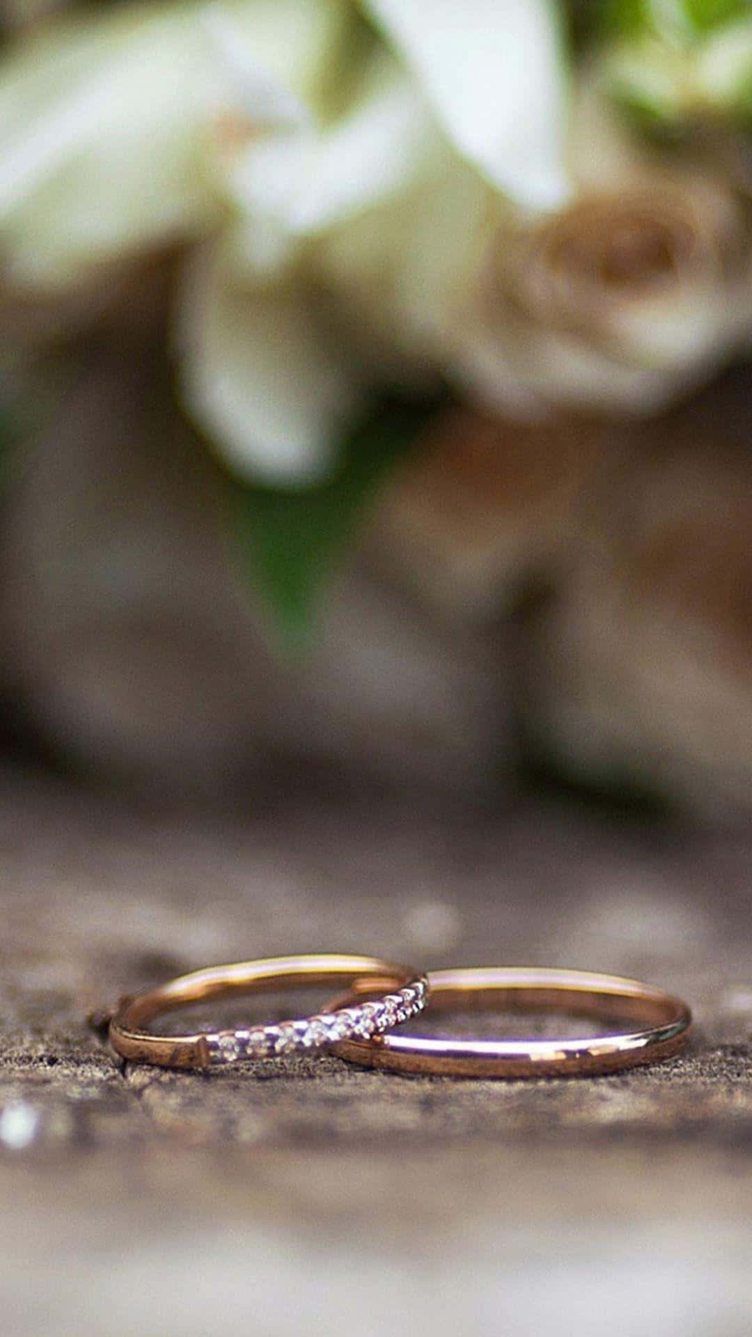 Wedding Rings 桌布 壁紙 — 兩枚玫瑰金結婚戒指放在風化木上，背景有柔和的白色花朵模糊。