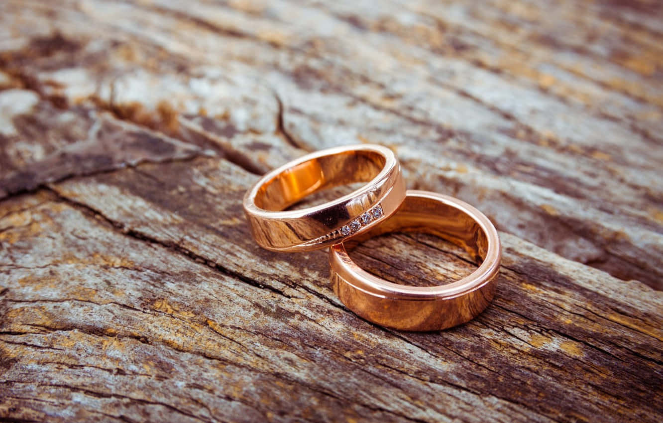 Marriage 桌布 壁紙 — 兩枚玫瑰金結婚戒指鑲有鑽石，親密地放在風化的木質表面上。