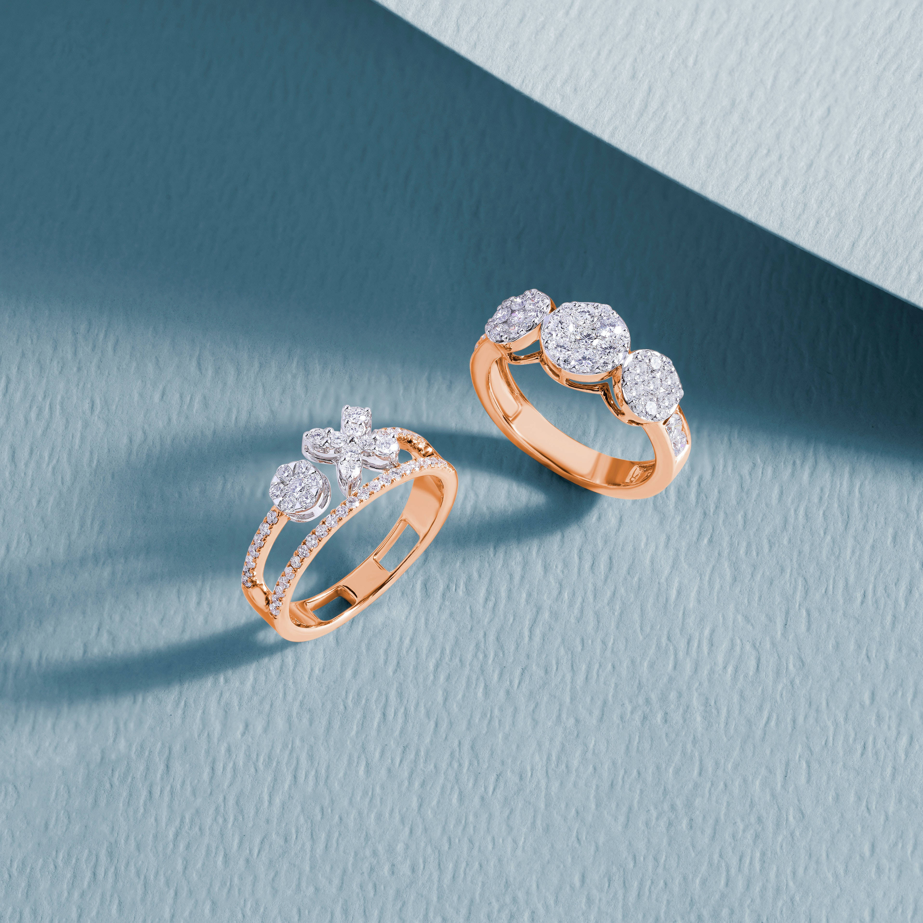 Gold Jewellery 桌布 壁紙 — 兩枚玫瑰金鑽石戒指，鑲嵌精緻，置於帶紋理的藍色表面上，柔和定向照明下。