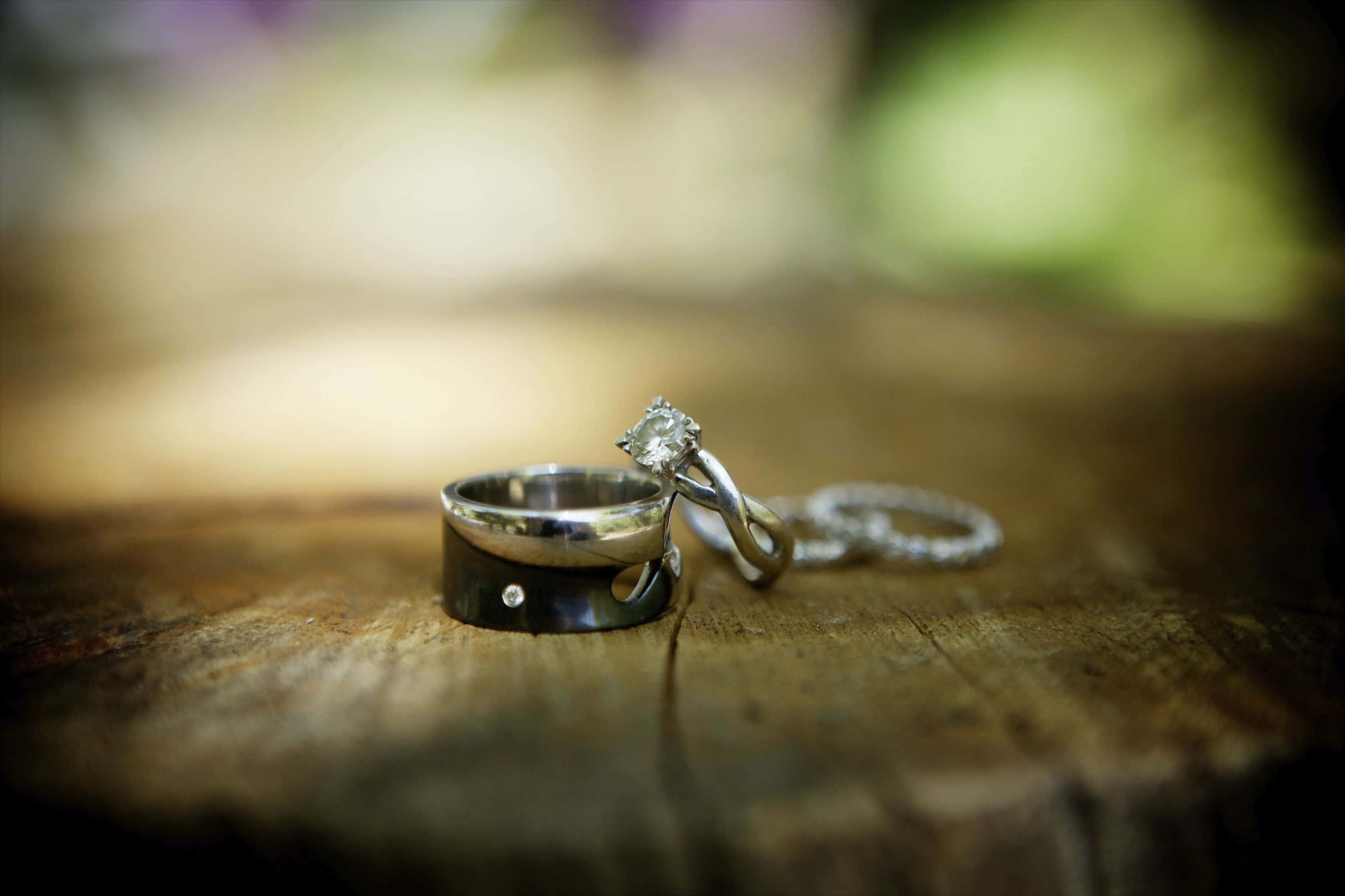 Wedding Rings 桌布 壁紙 — 兩枚結婚戒指，一枚鑲有大鑽石，一枚素面，放在質樸的木質表面上，背景柔和模糊。