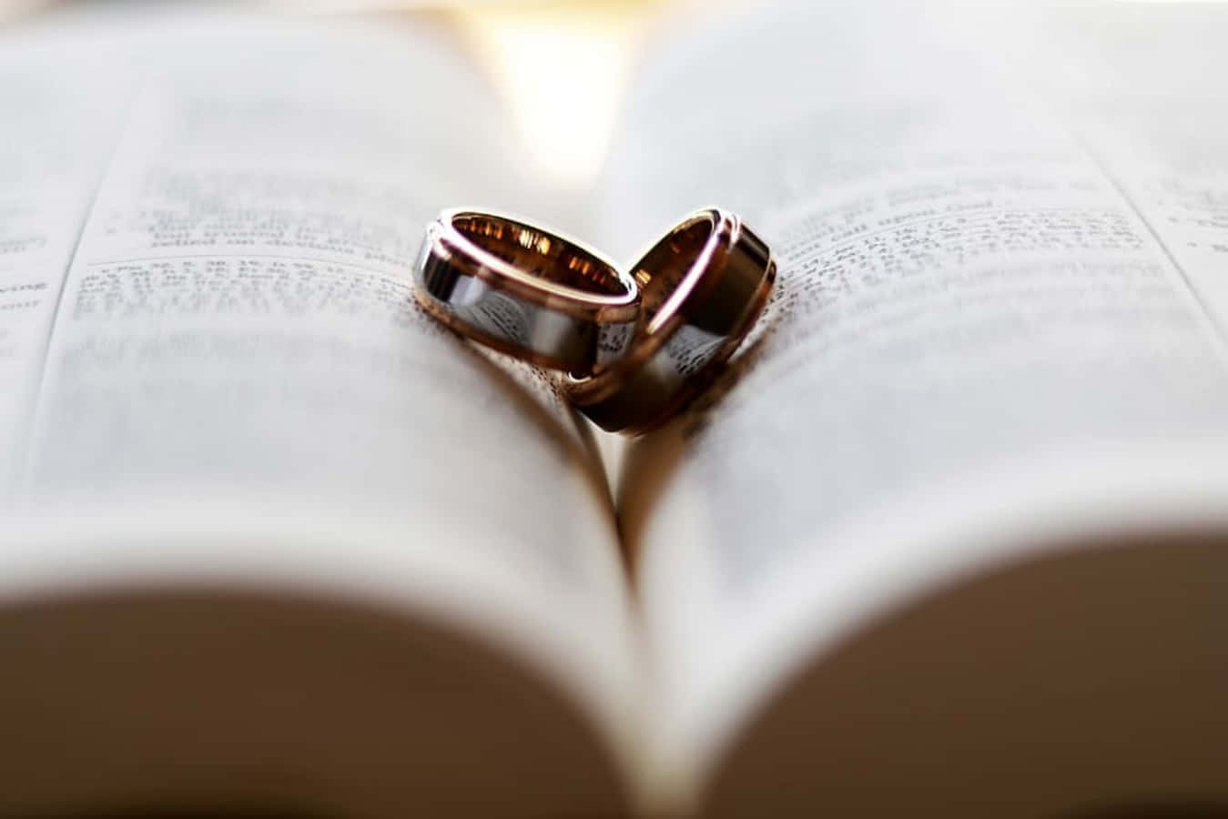 結婚戒指 桌布 壁紙 — 兩枚結婚戒指以心形放置在打開的書本上，柔和溫暖的光線突顯其金屬光澤。